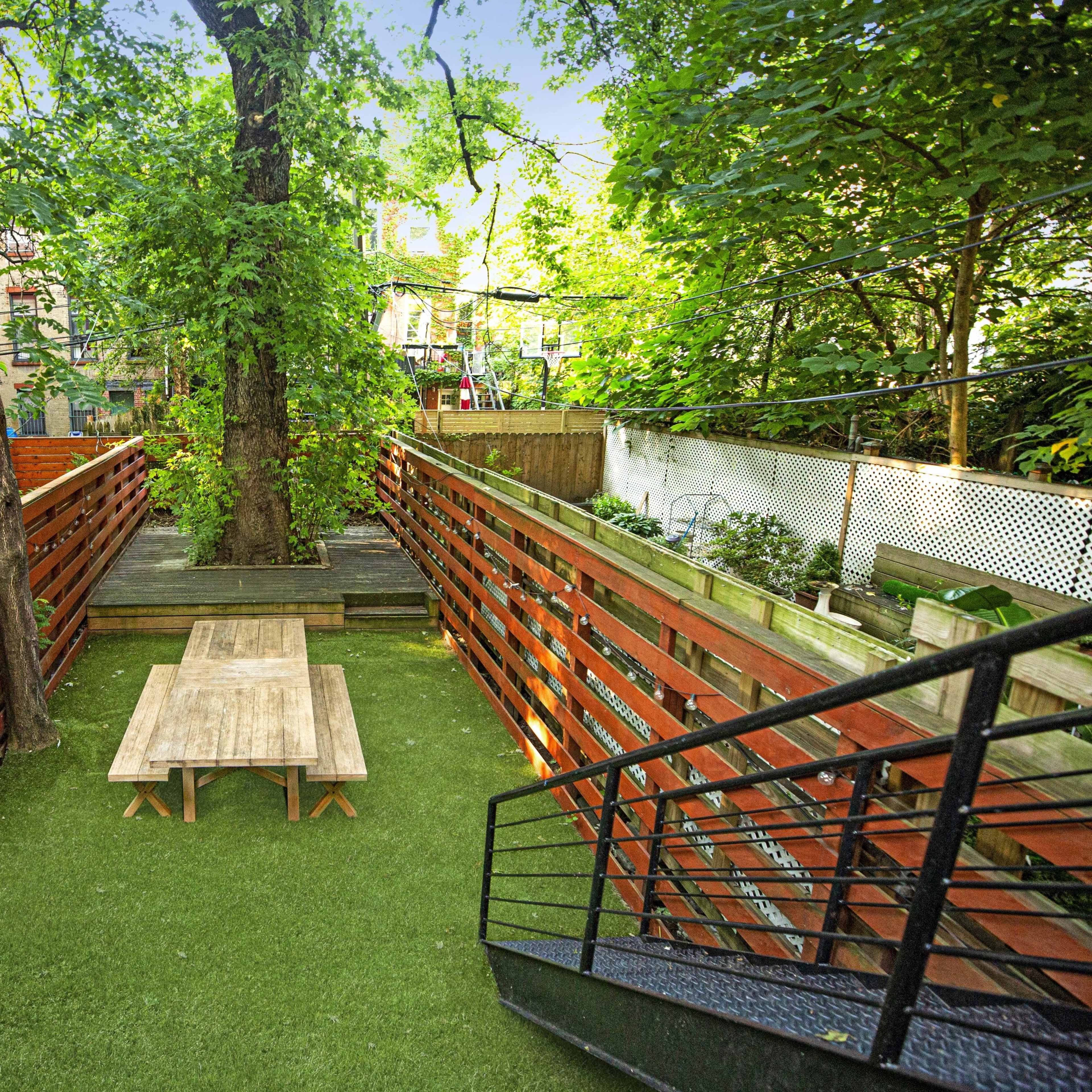 A wooden platform with a table surrounded by greenery and a staircase leading down to a lower area.