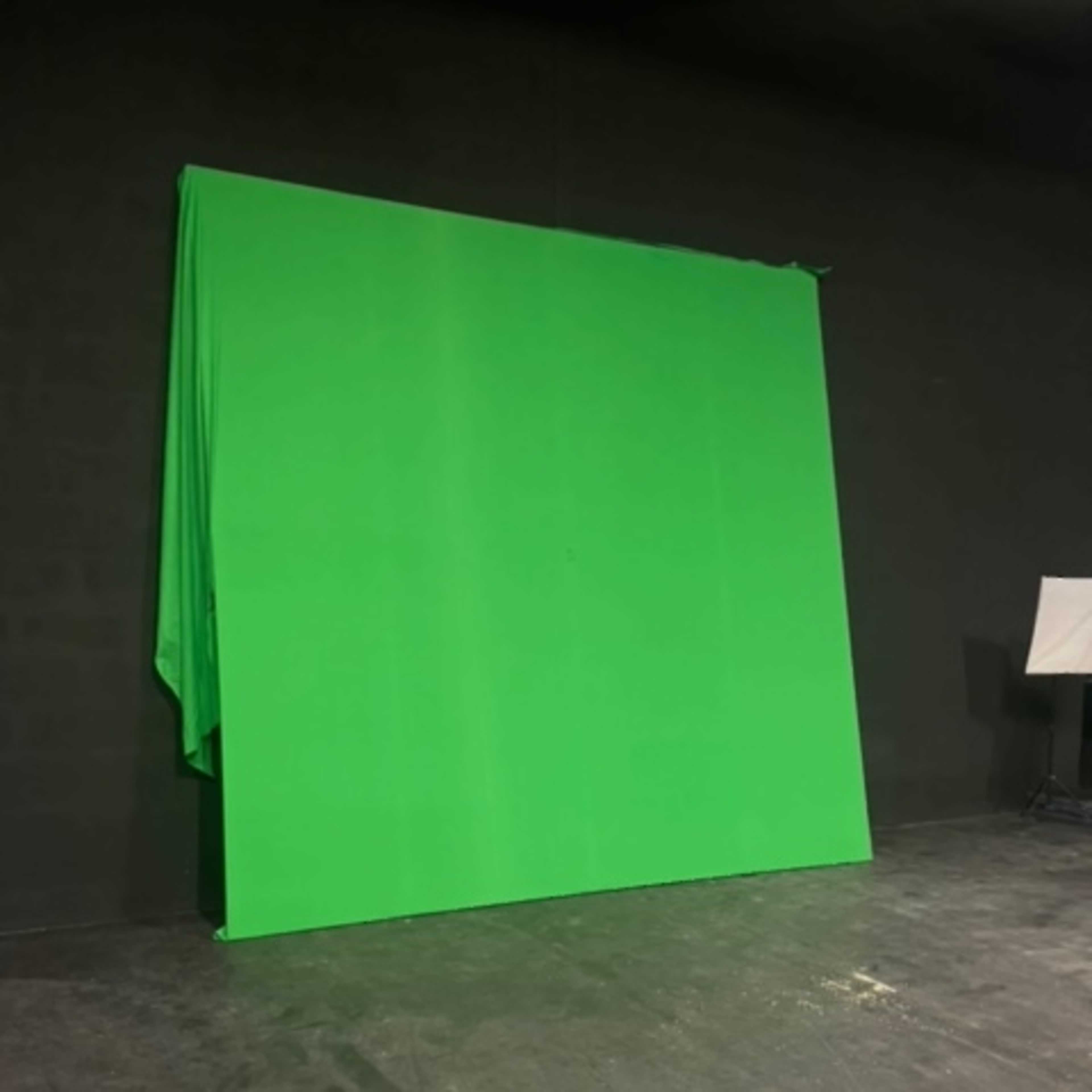 A large green screen set up against a black wall in a studio environment.