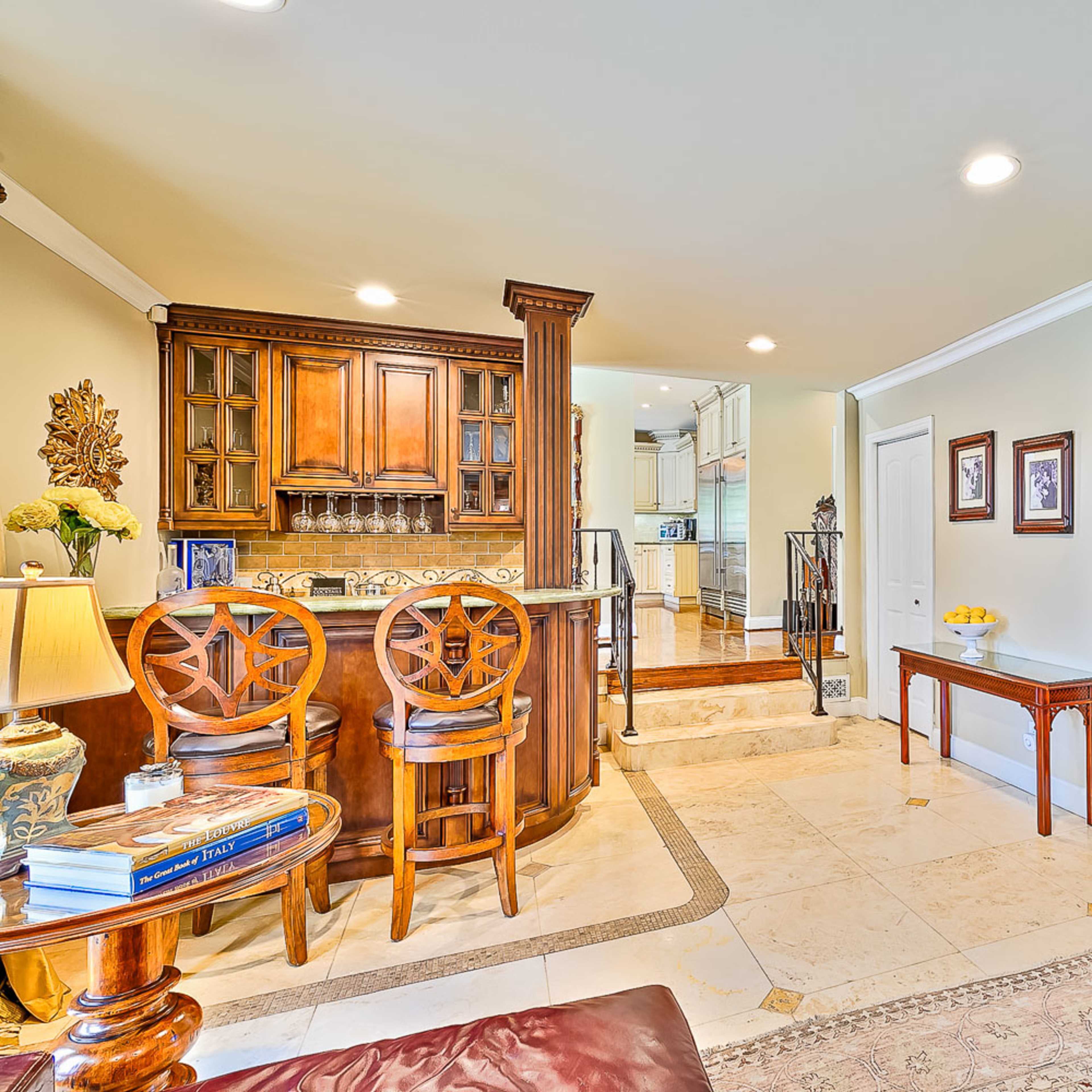 A spacious living area featuring a bar with high stools, a staircase leading to another room, and a grand piano positioned near a decorative table.