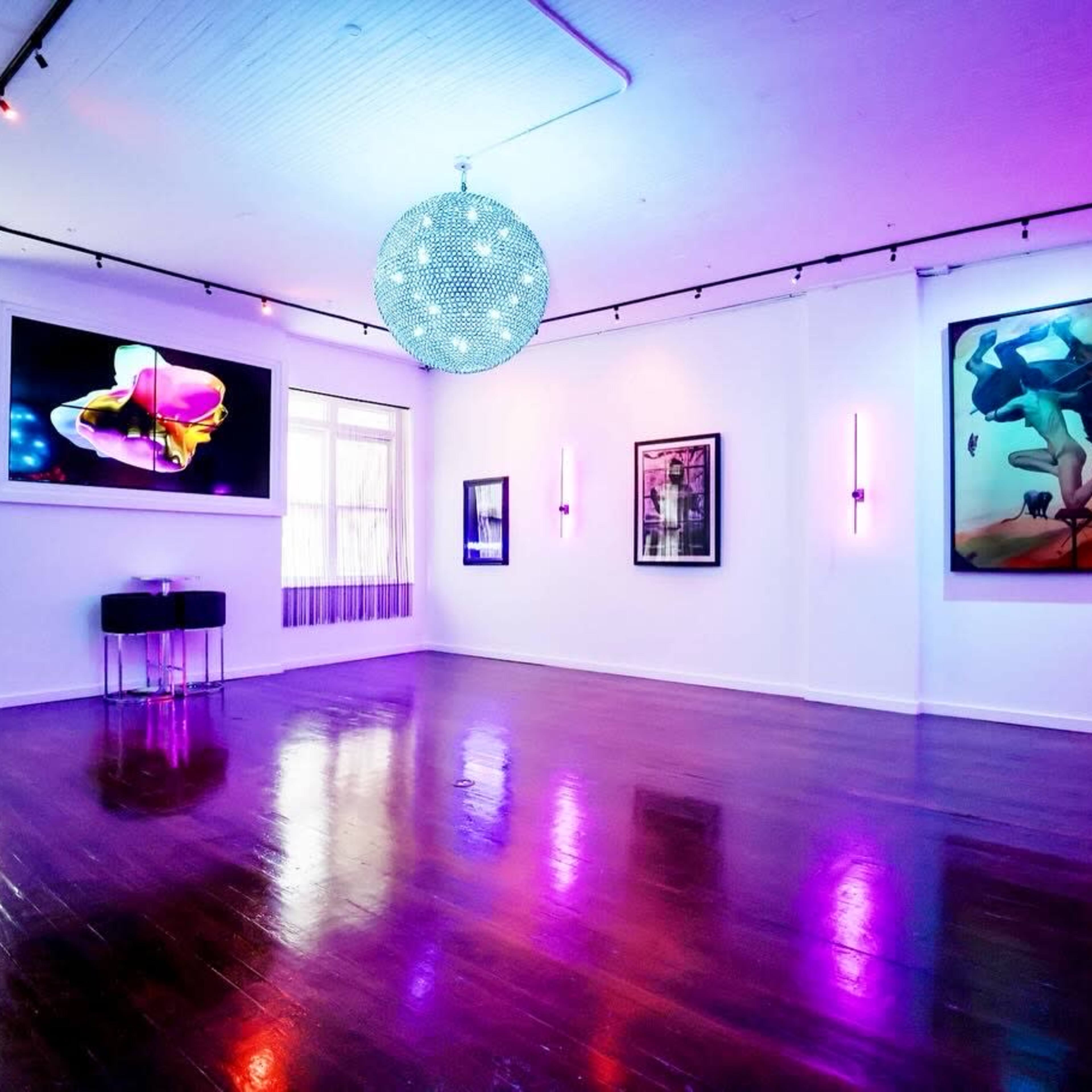A modern art gallery with dim lighting, featuring colorful artworks on the walls and a large disco ball hanging from the ceiling.