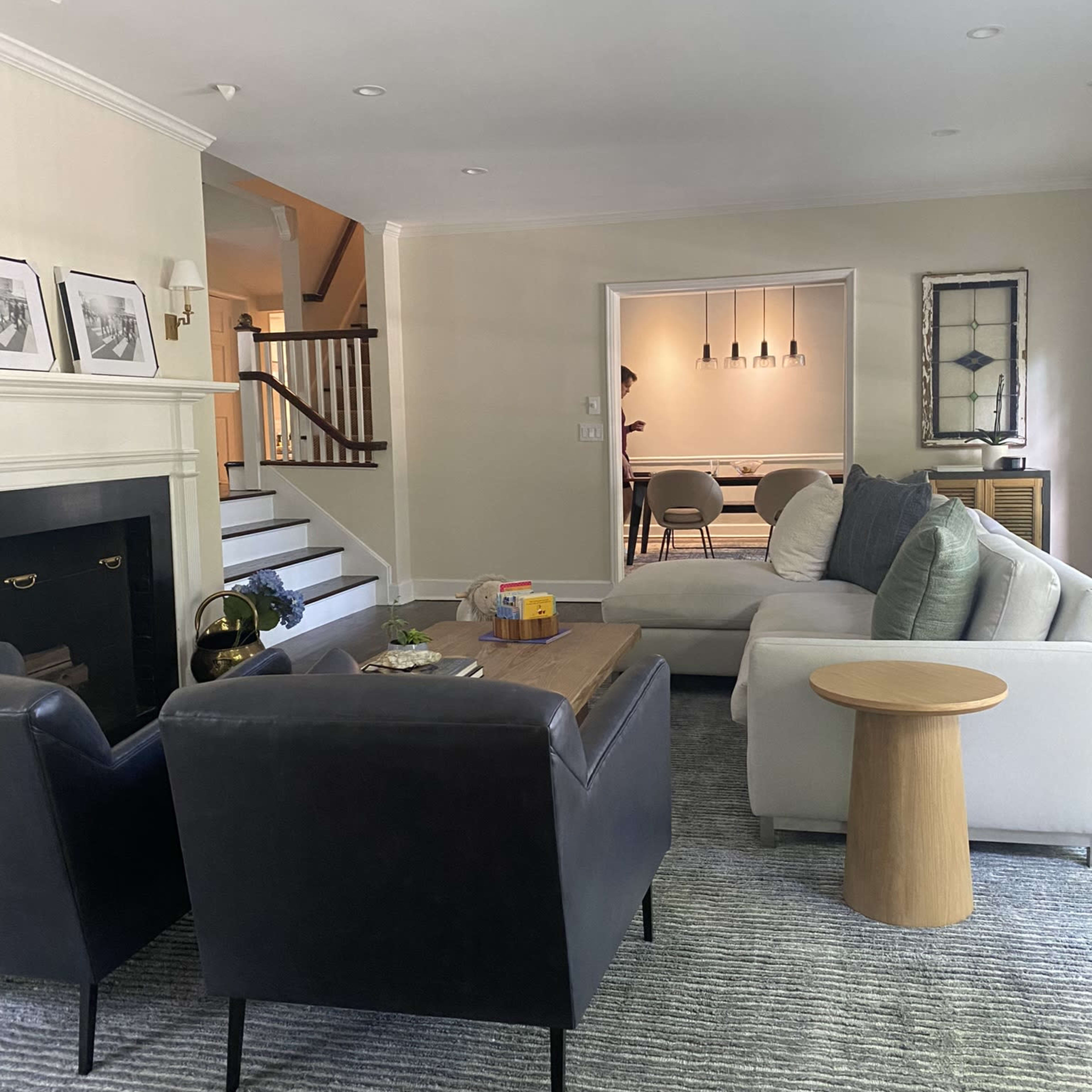 A cozy living room with a black leather chair, a light-colored sofa, a wooden coffee table, and a view of a dining area through an open doorway.