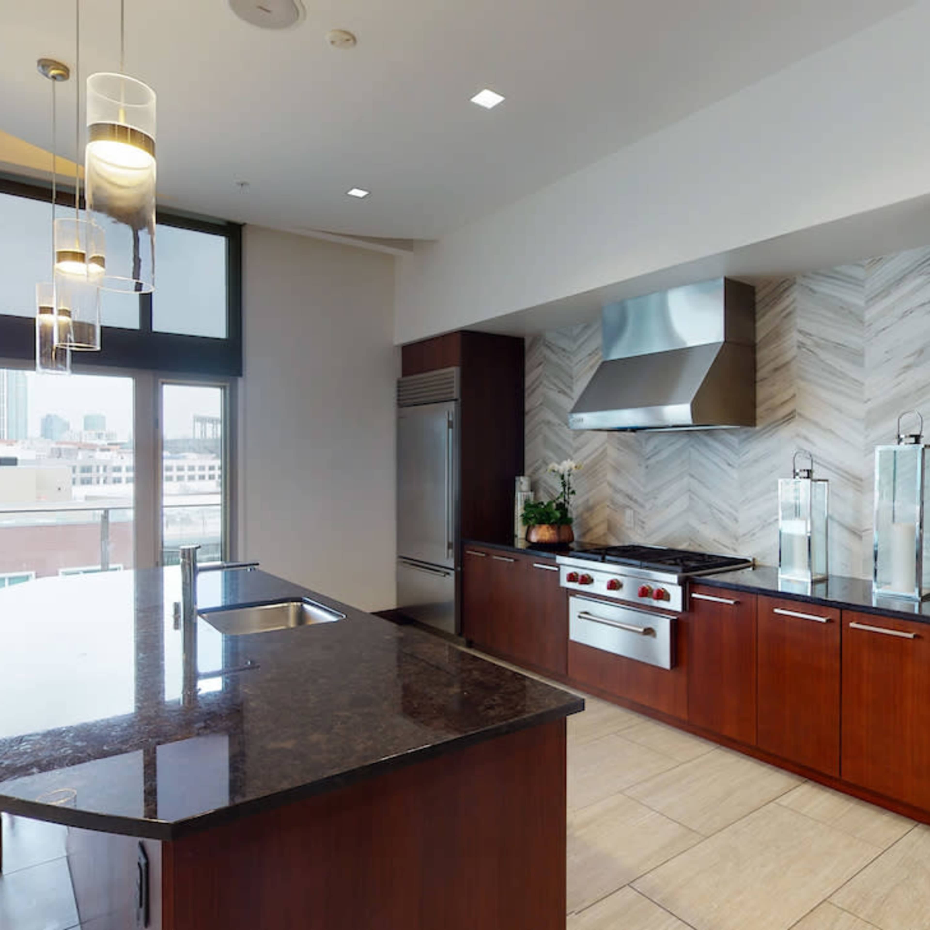 A modern kitchen features a large island with seating, stainless steel appliances, and a sleek backsplash with a city skyline visible through the windows.