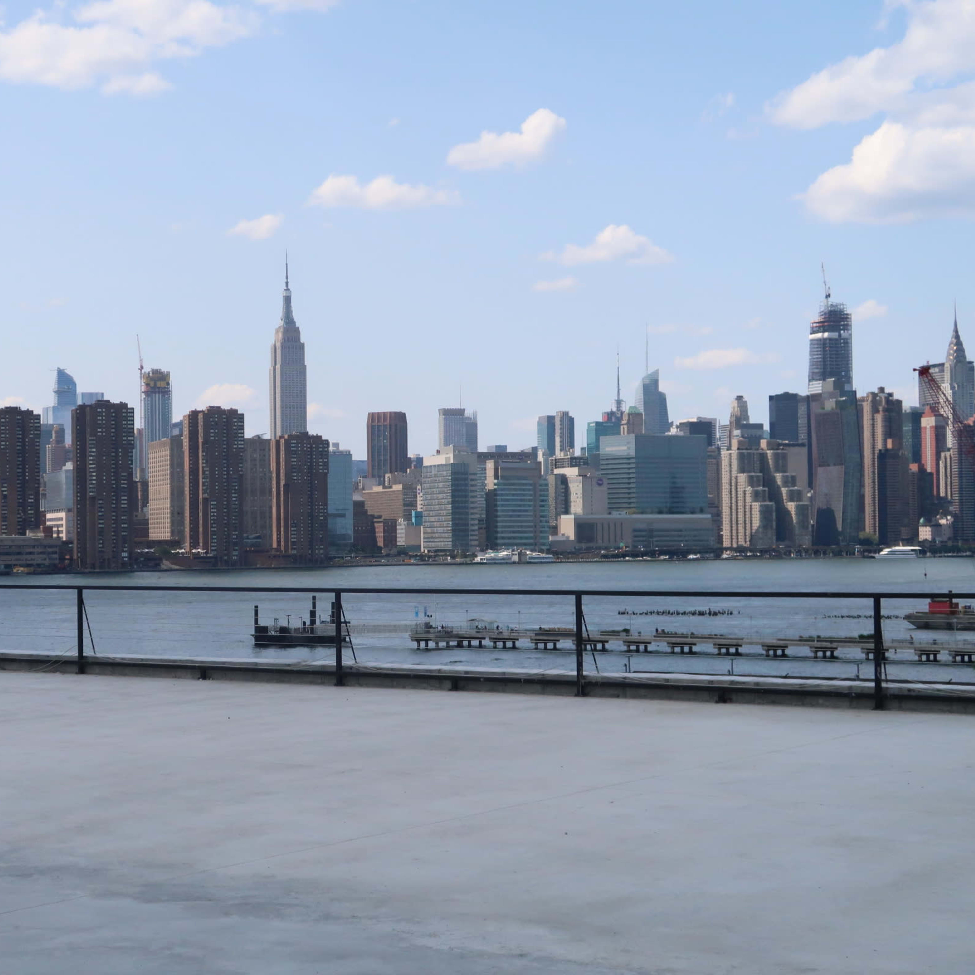 A wide view of the New York City skyline from a waterfront location, with the Empire State Building prominently visible among other skyscrapers.