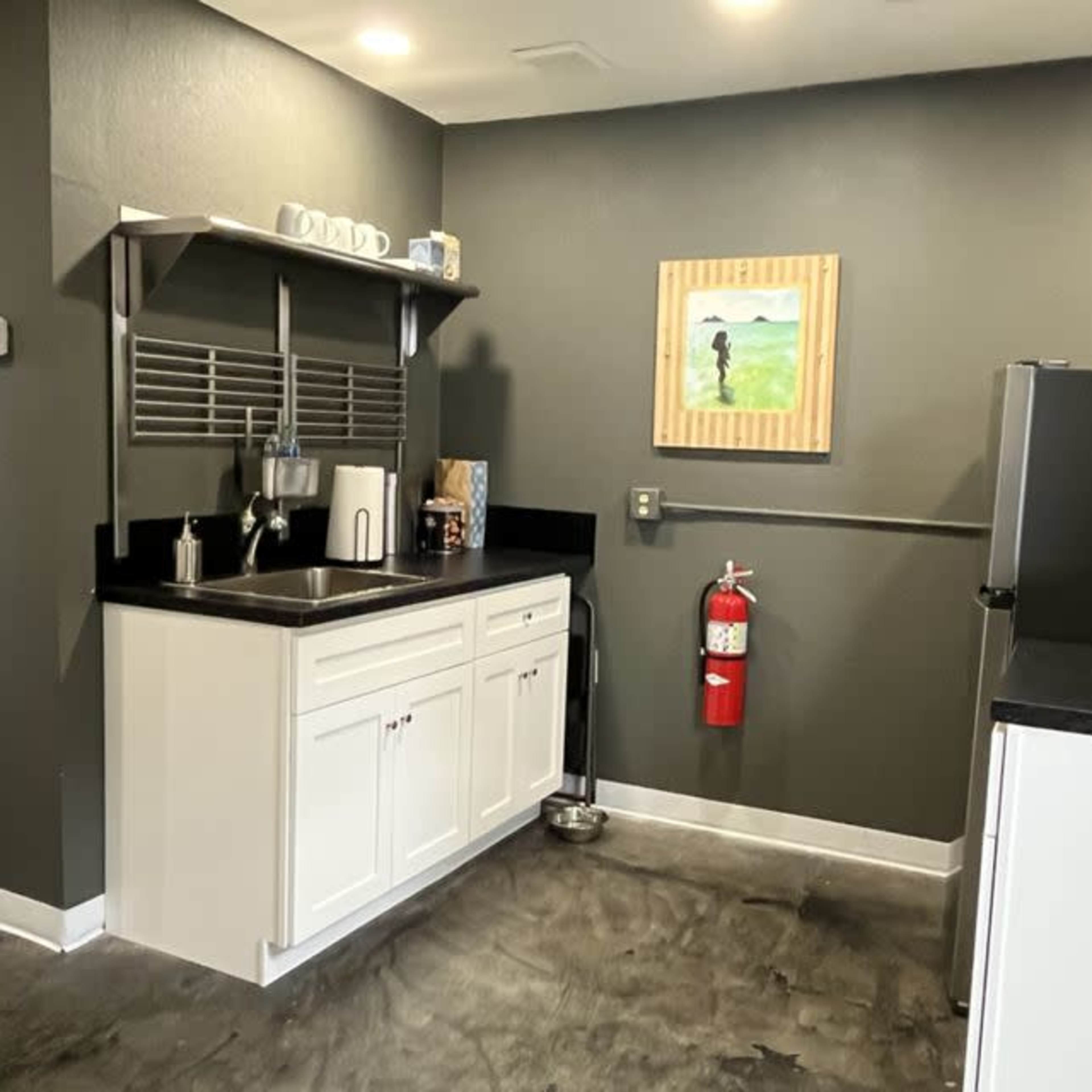 A kitchen area with white cabinets, a black countertop, and a fire extinguisher mounted on the wall.