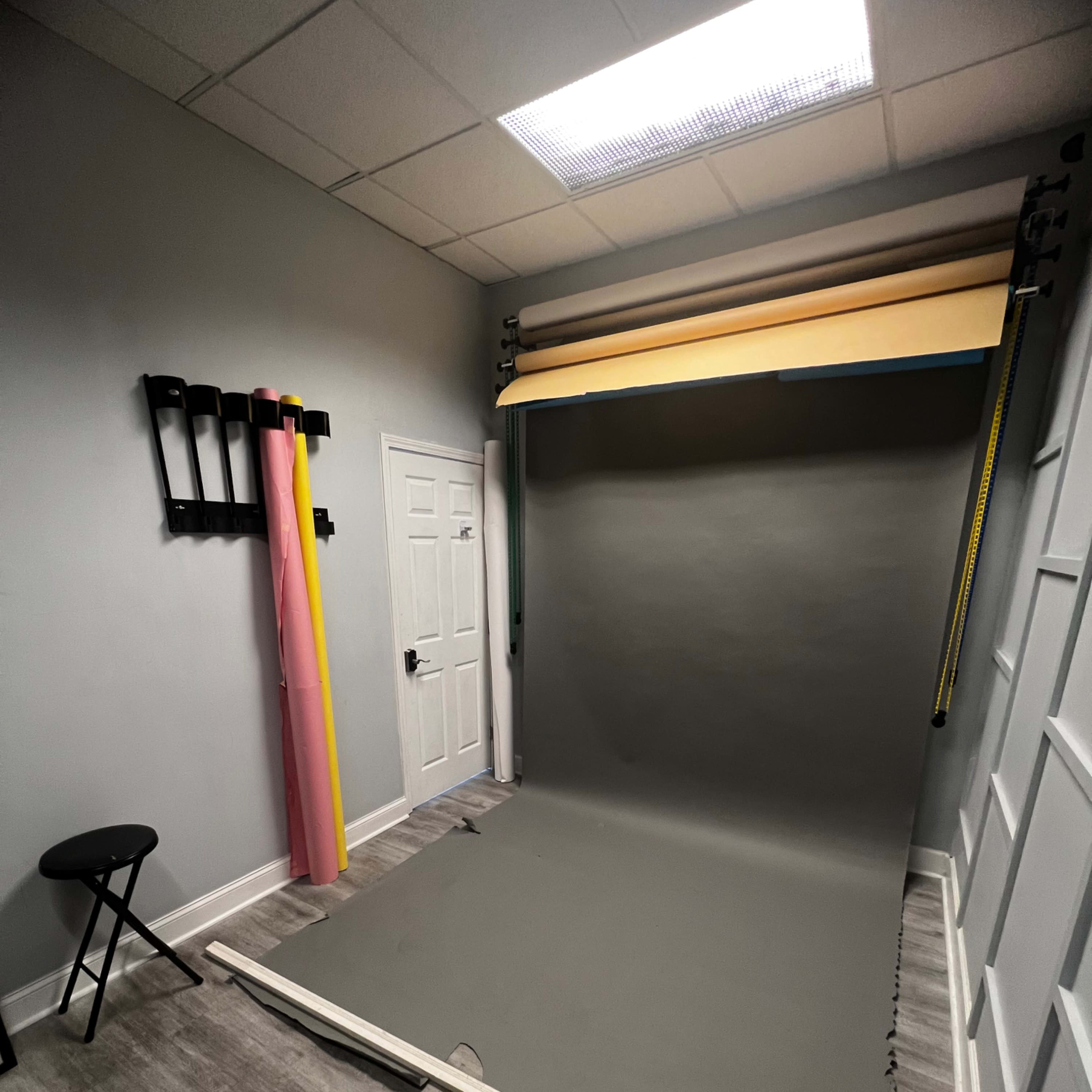 A photography studio with a gray backdrop, a stool, and colorful roll-up backdrops hanging on the wall.