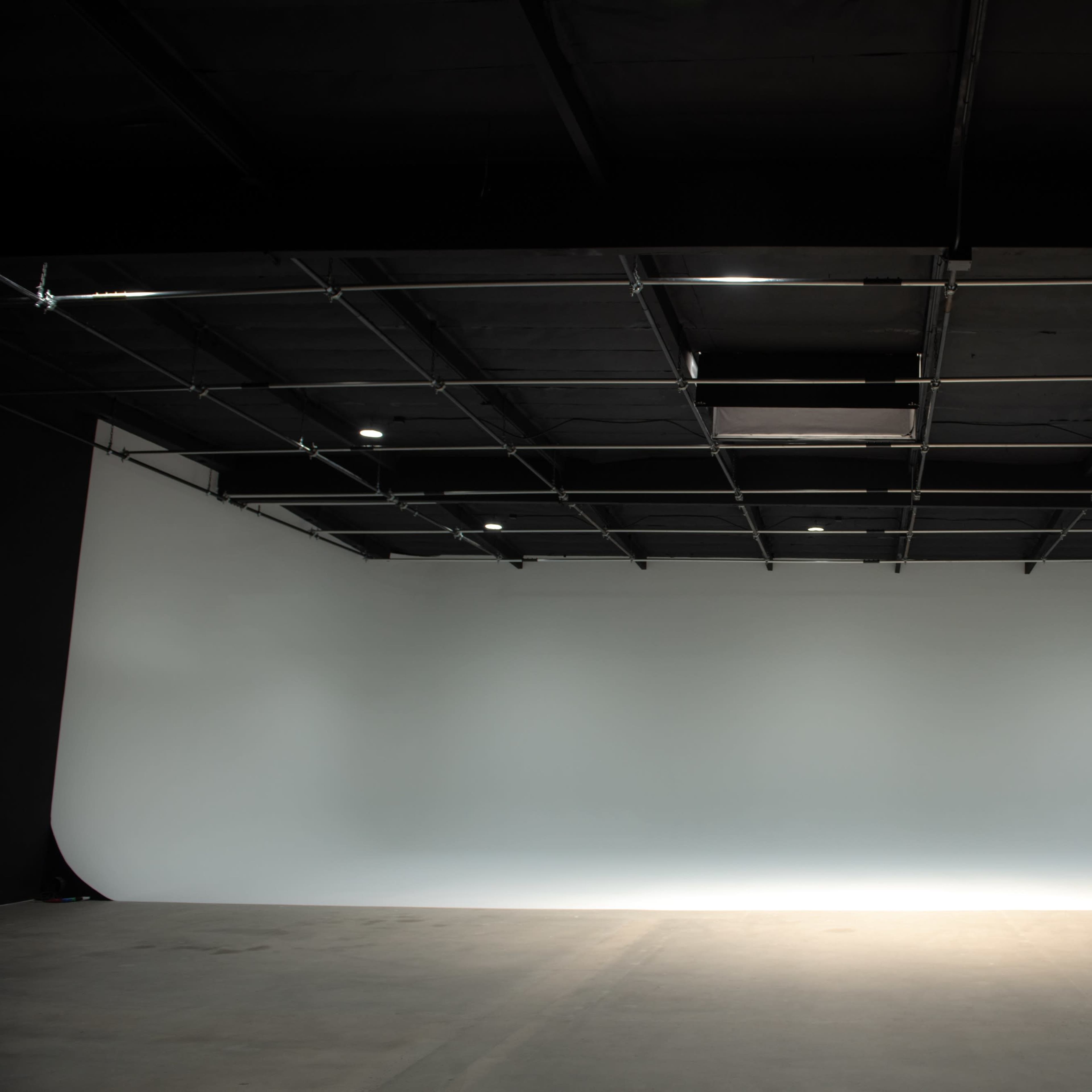 A spacious photography studio with a seamless backdrop and overhead lighting.