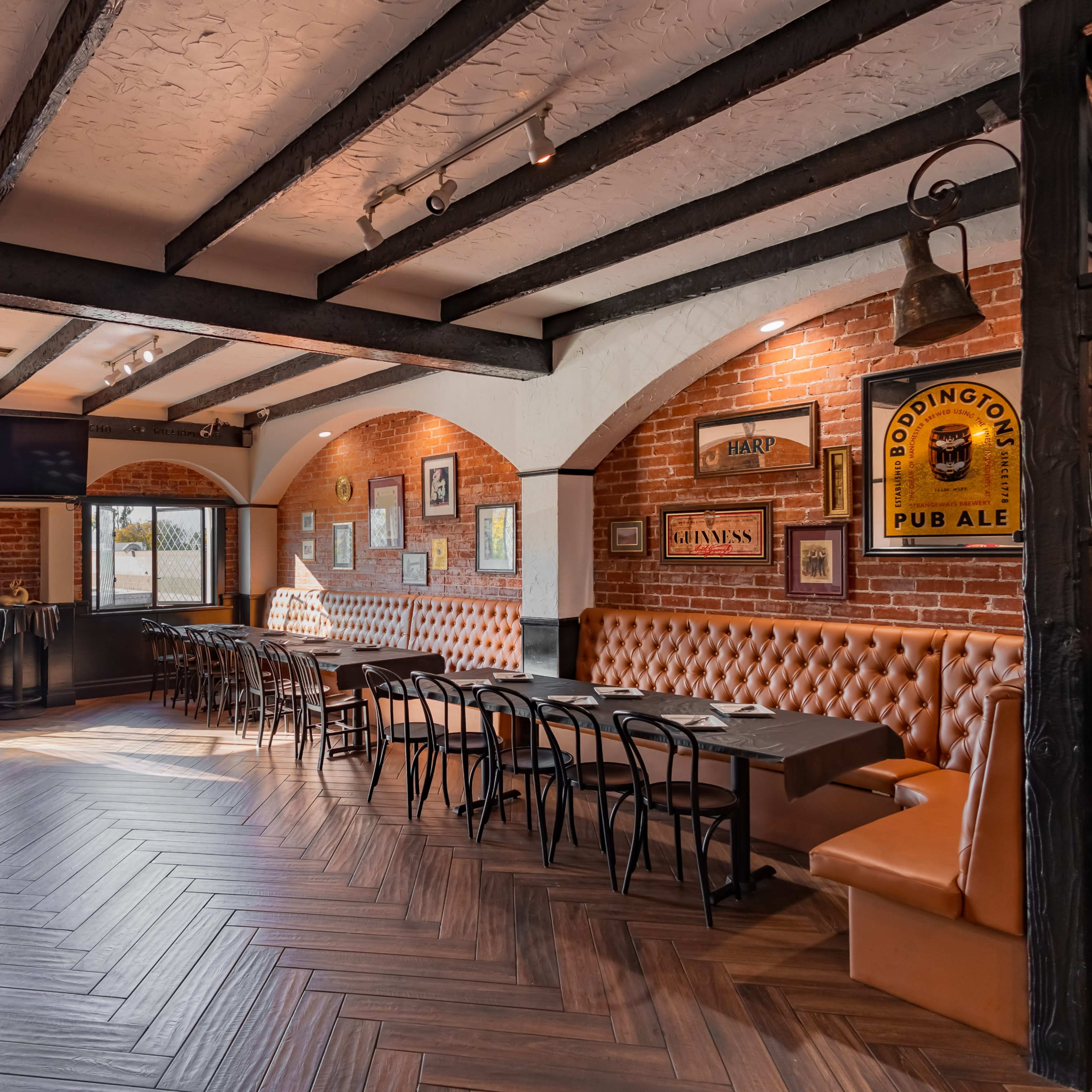 A restaurant interior with wooden beams, brick walls, and a mix of seating options including upholstered benches and dining tables.