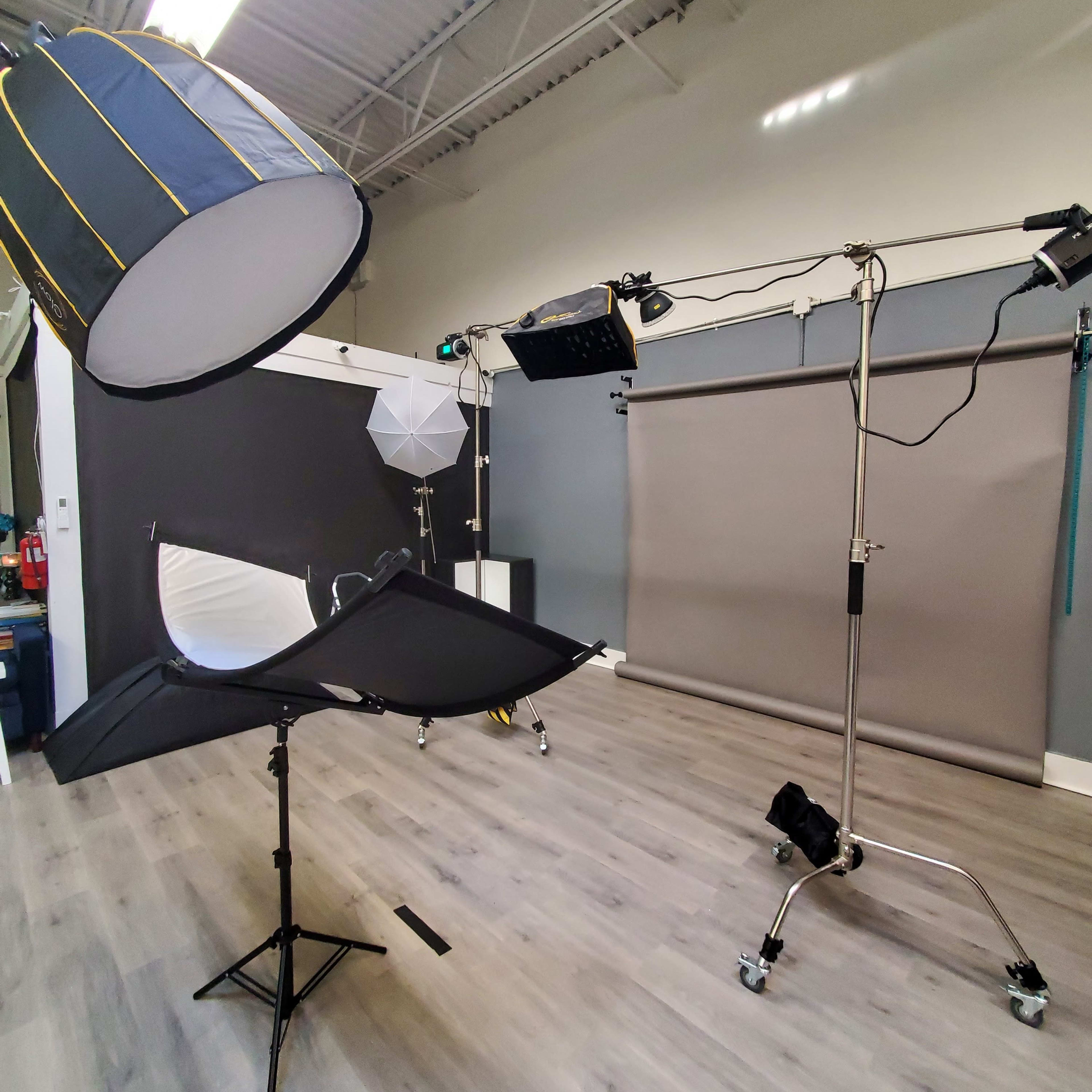 A photography studio equipped with lighting equipment, including a large softbox and a reflector on stands, along with a backdrop setup.