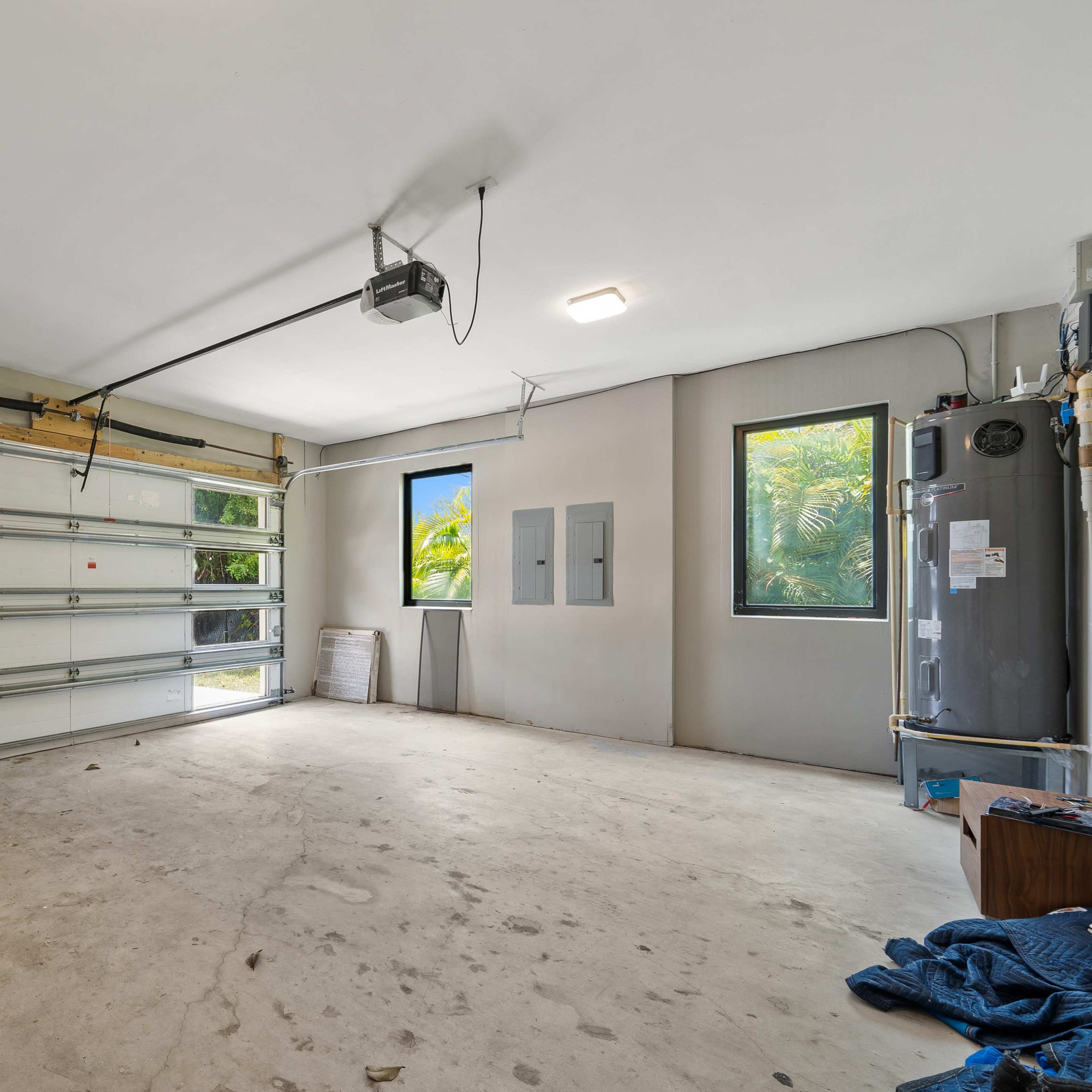 A spacious and empty garage with two windows, a garage door, and utility panels on the wall.