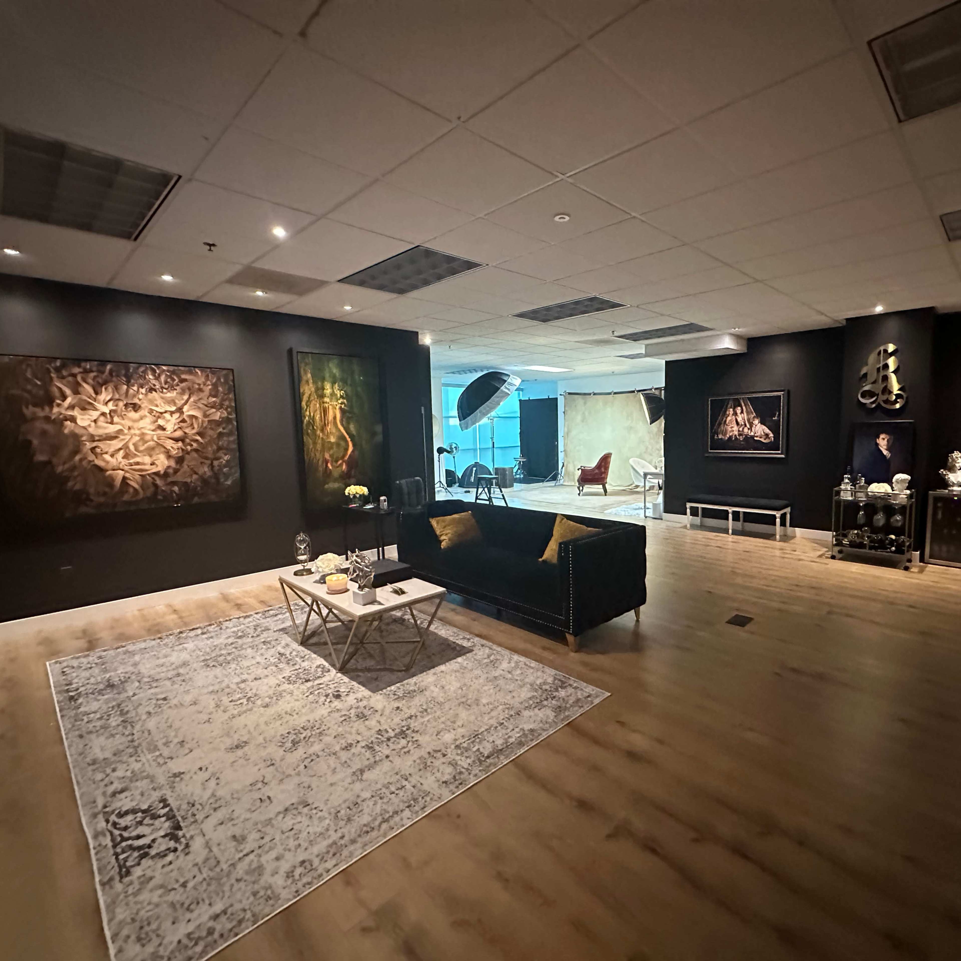 A spacious art gallery featuring black walls adorned with various paintings, a central seating area with a coffee table, and a light source illuminating the space.