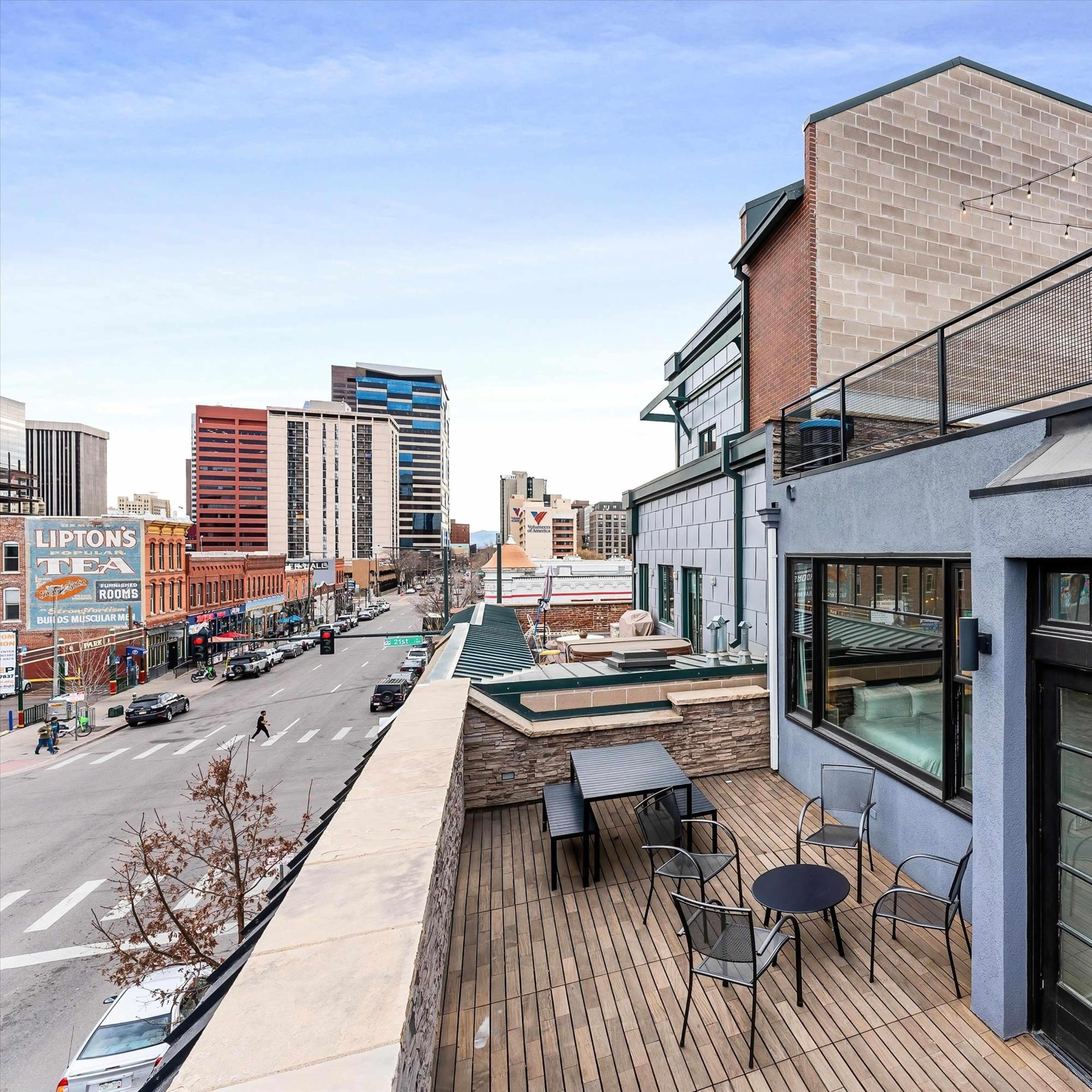 A rooftop terrace with outdoor seating overlooking a city street lined with buildings and a sign for Lipton's Tea.