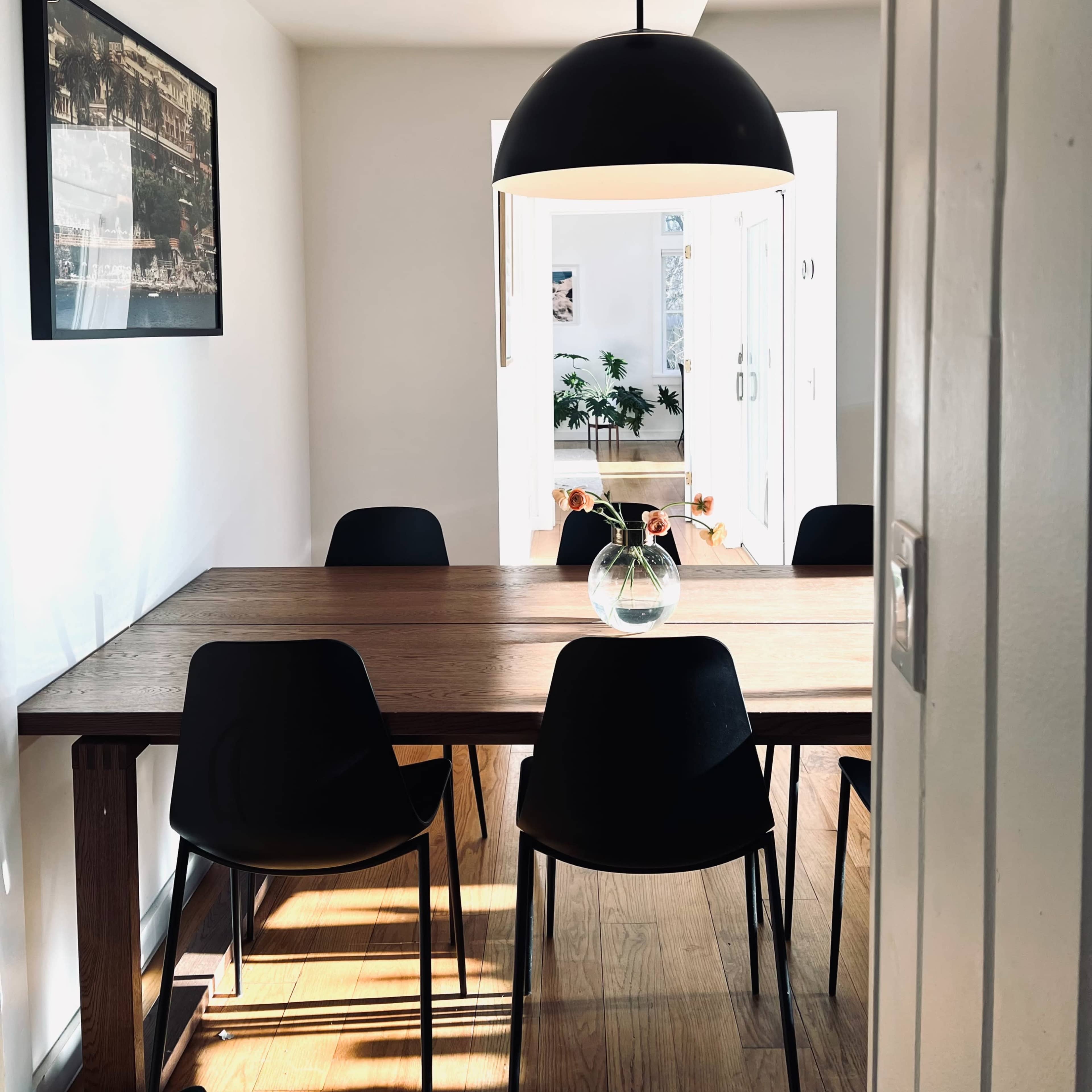 A modern dining area features a wooden table surrounded by black chairs and illuminated by a large black pendant light.
