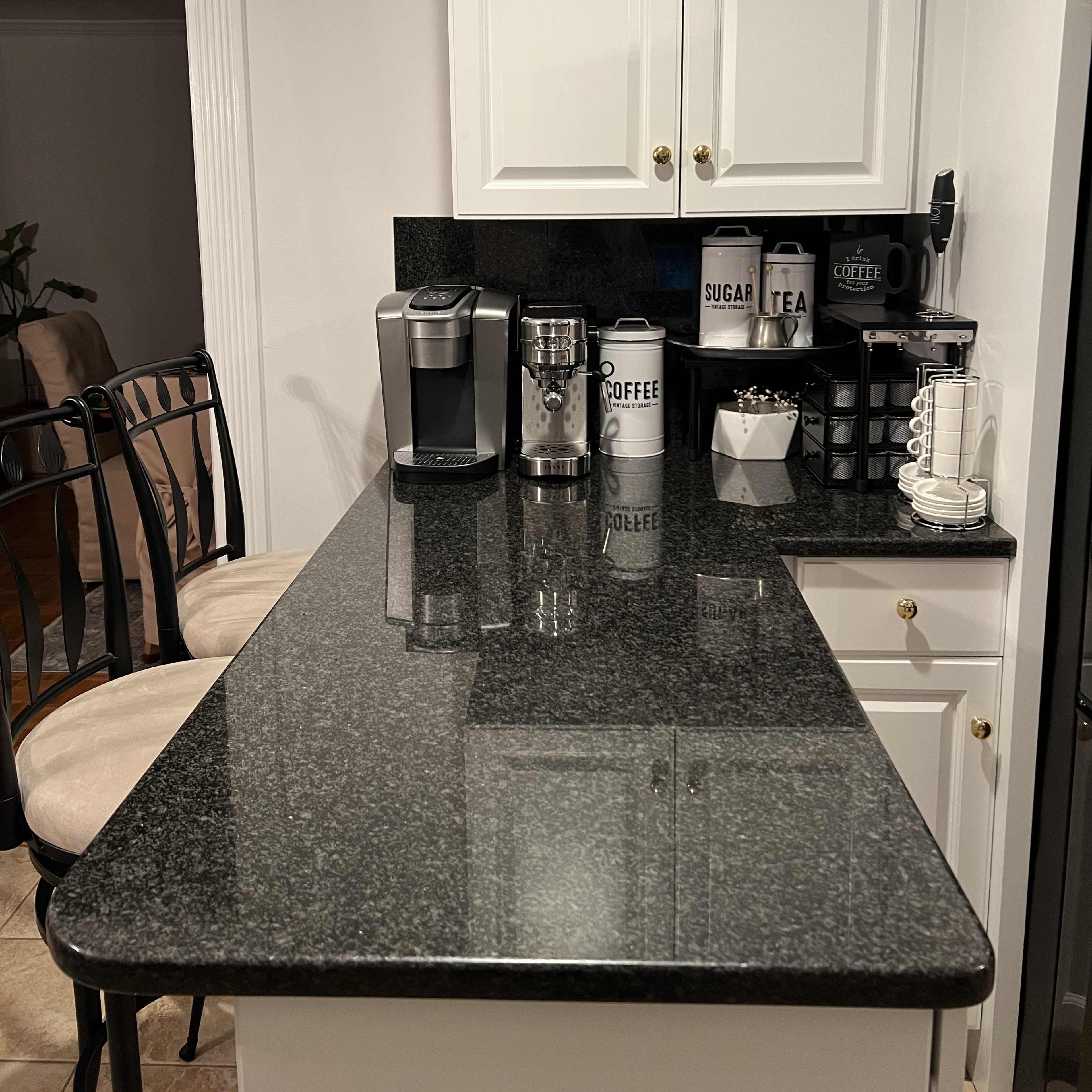 A kitchen countertop with a coffee maker, a grinder, storage canisters, and bar stools.