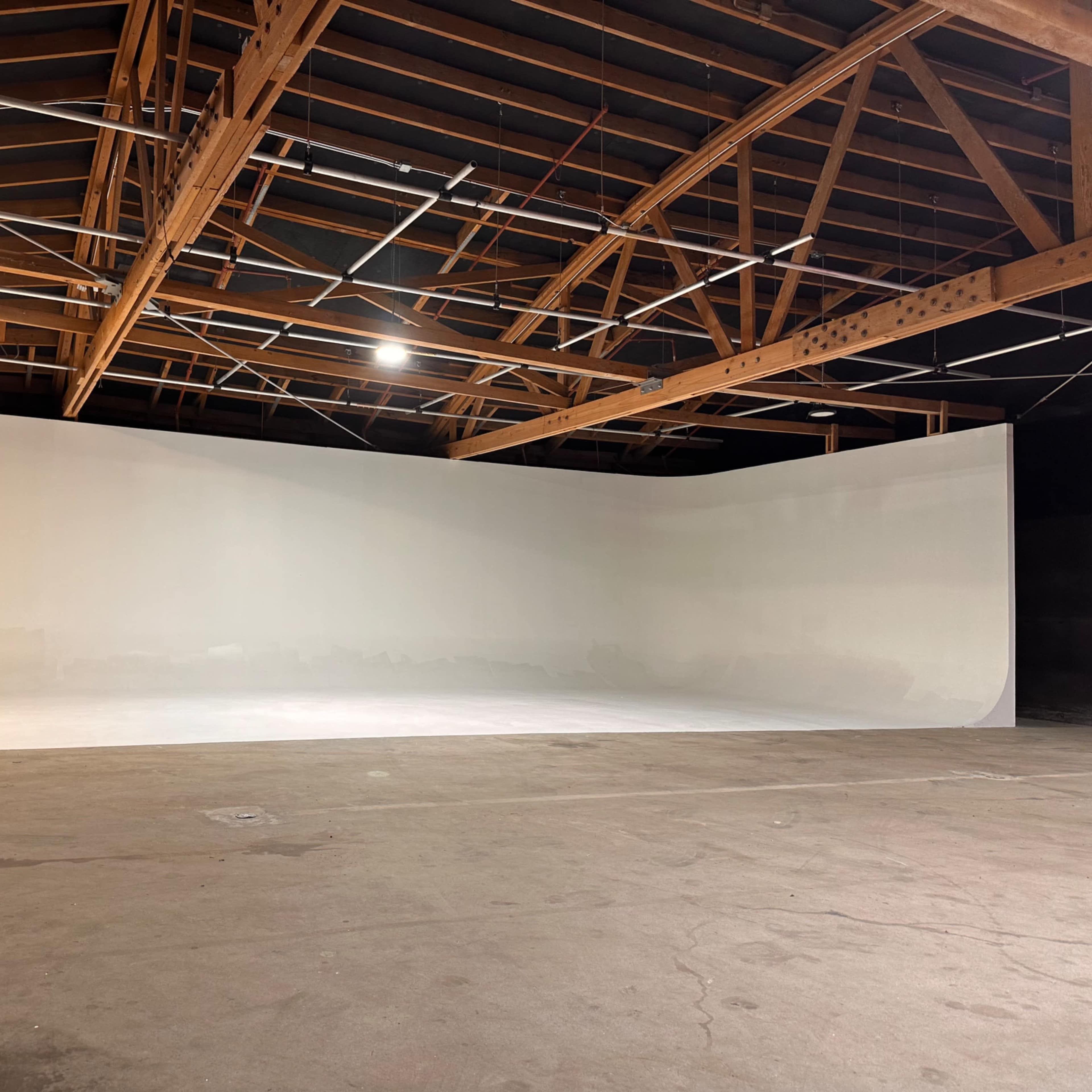 A spacious studio with a smooth white backdrop and a wooden-beamed ceiling.
