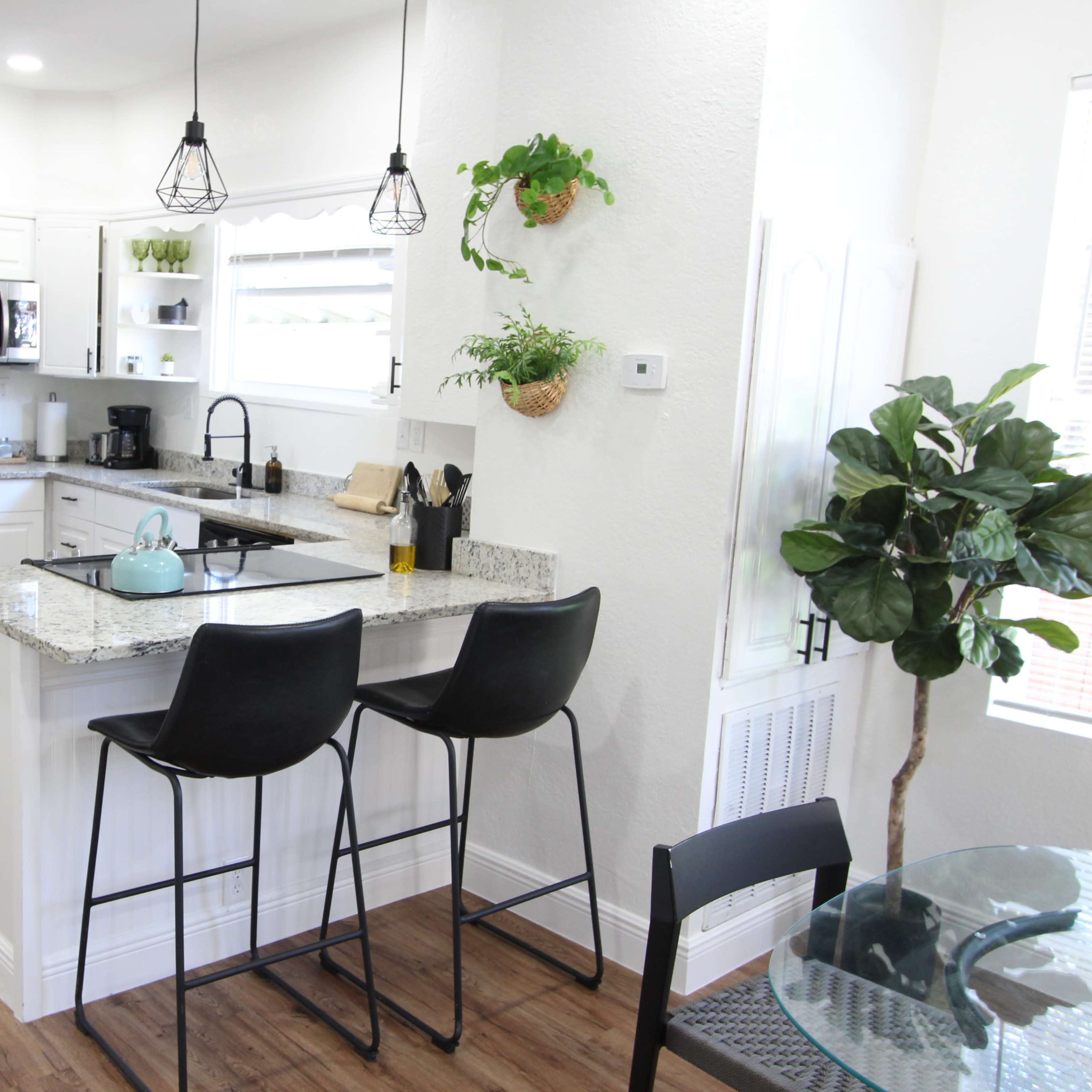 A modern kitchen features stainless steel appliances, granite countertops, and a small breakfast bar with two stools.