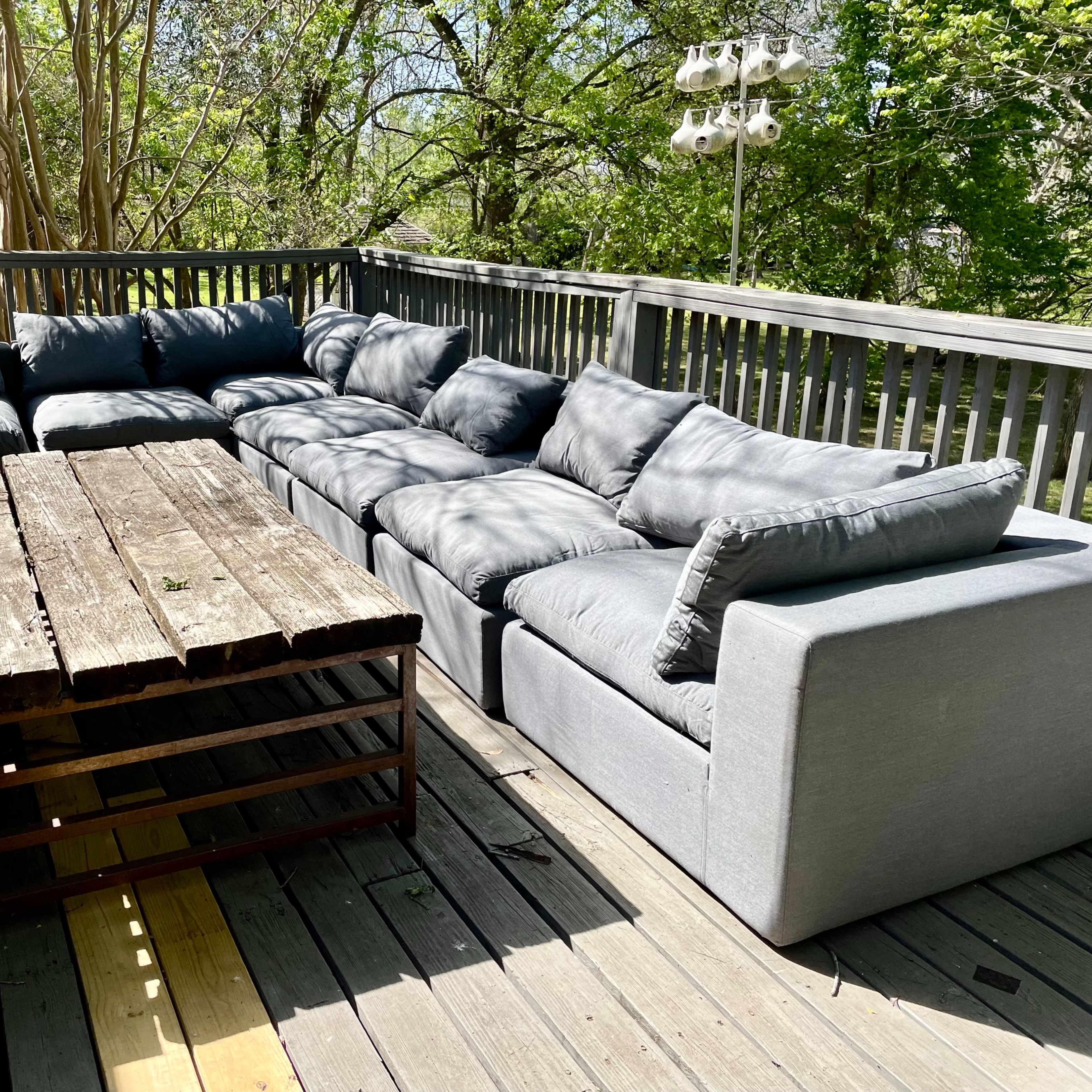 A spacious outdoor deck featuring a large sectional sofa and a wooden coffee table made from reclaimed wood.