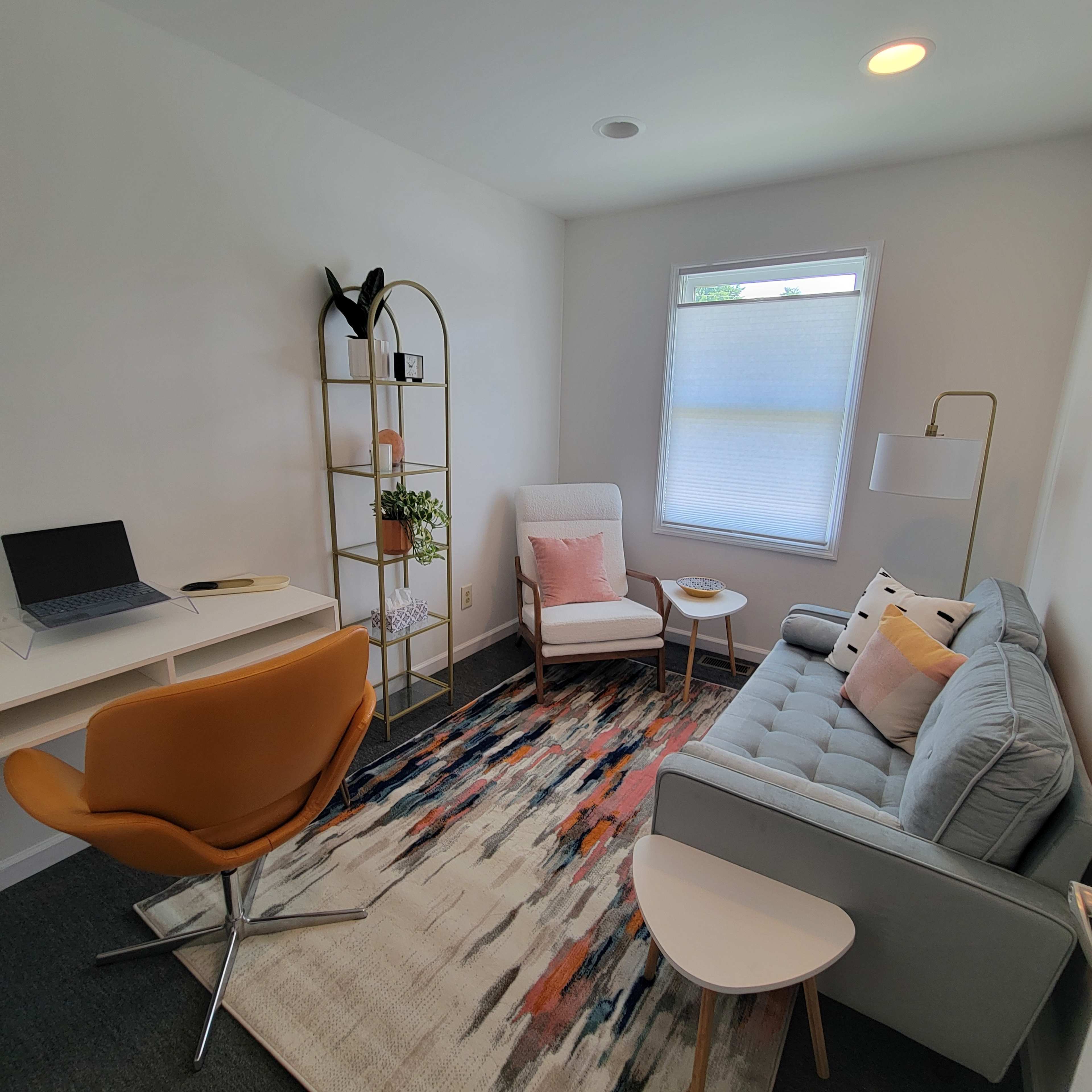 A modern living space with a gray sofa, an armchair, a small table, and a decorative shelf, all arranged around a colorful area rug.