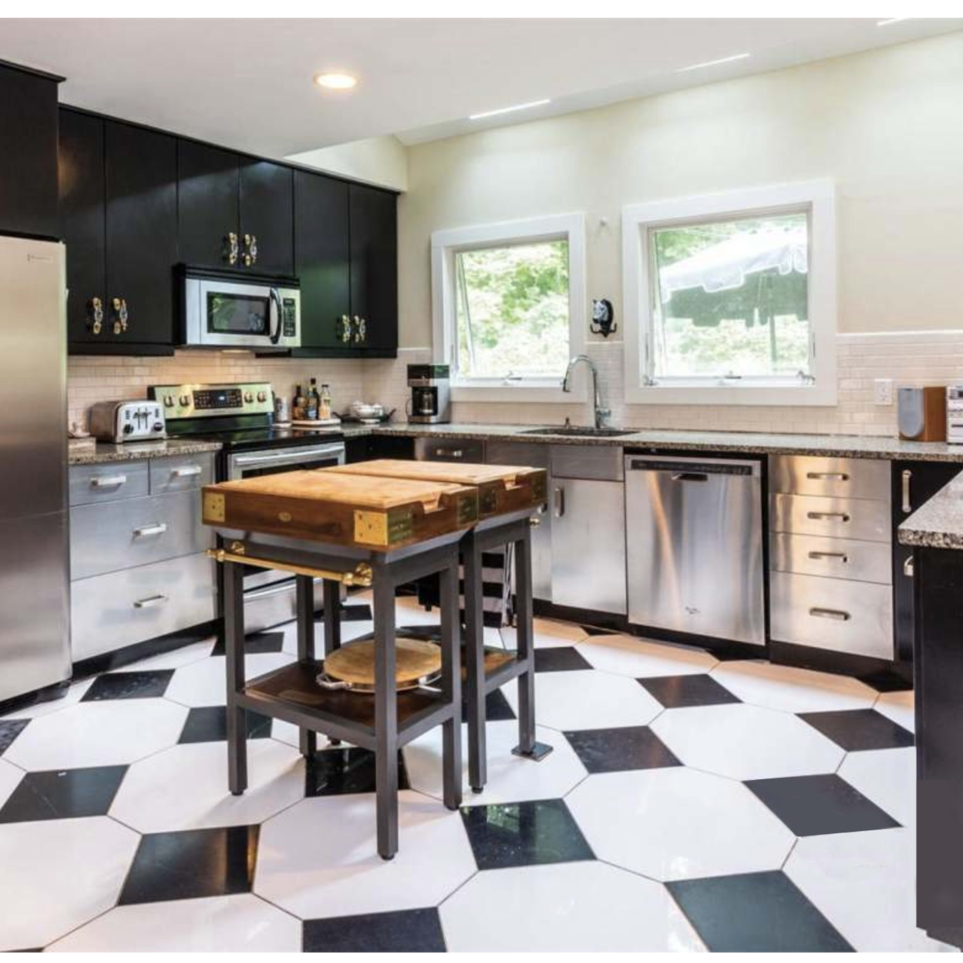 The kitchen features black cabinetry, stainless steel appliances, and a hexagonal black-and-white tiled floor with a central wooden island.