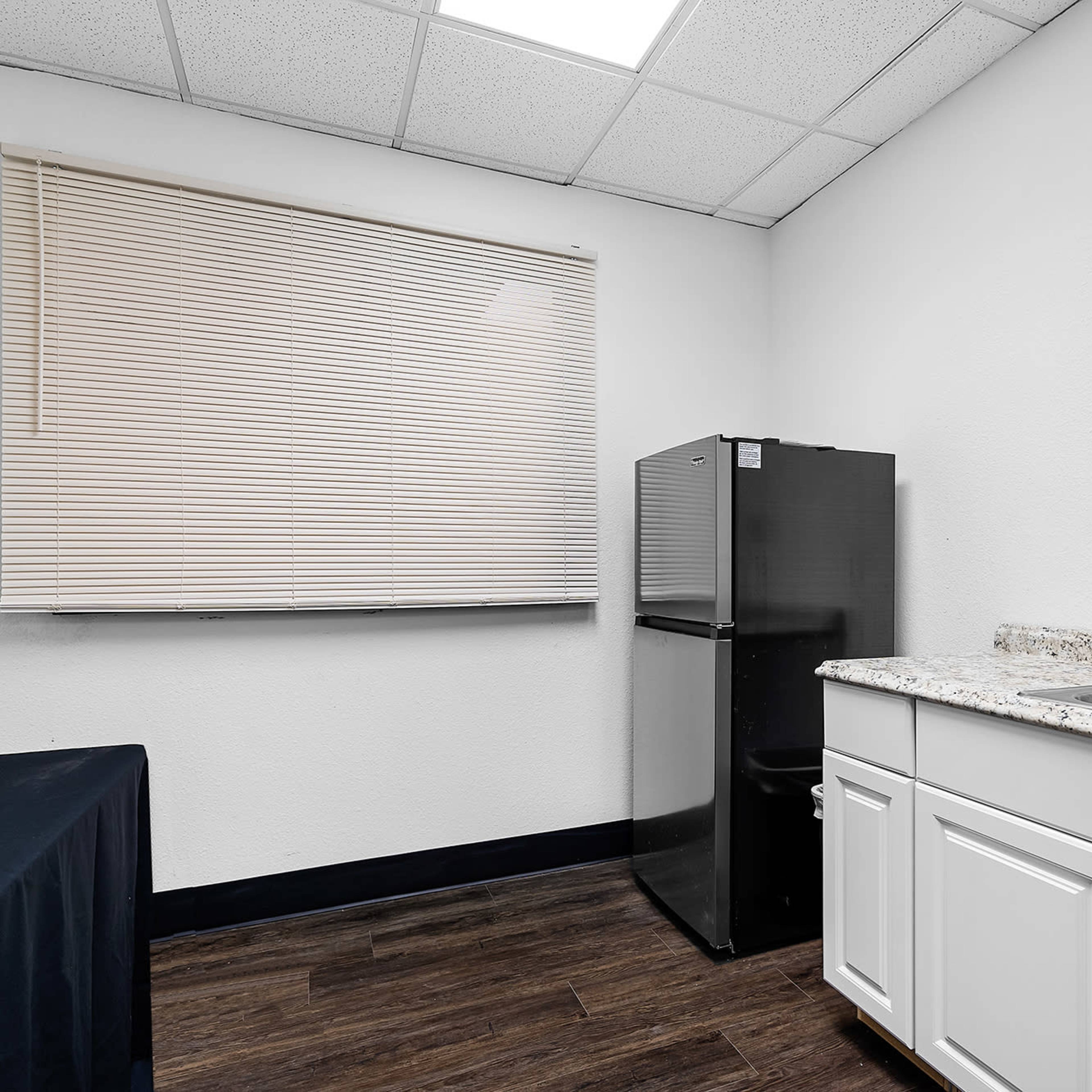 A small kitchen area with a refrigerator, a sink, and a window covered by a blind.
