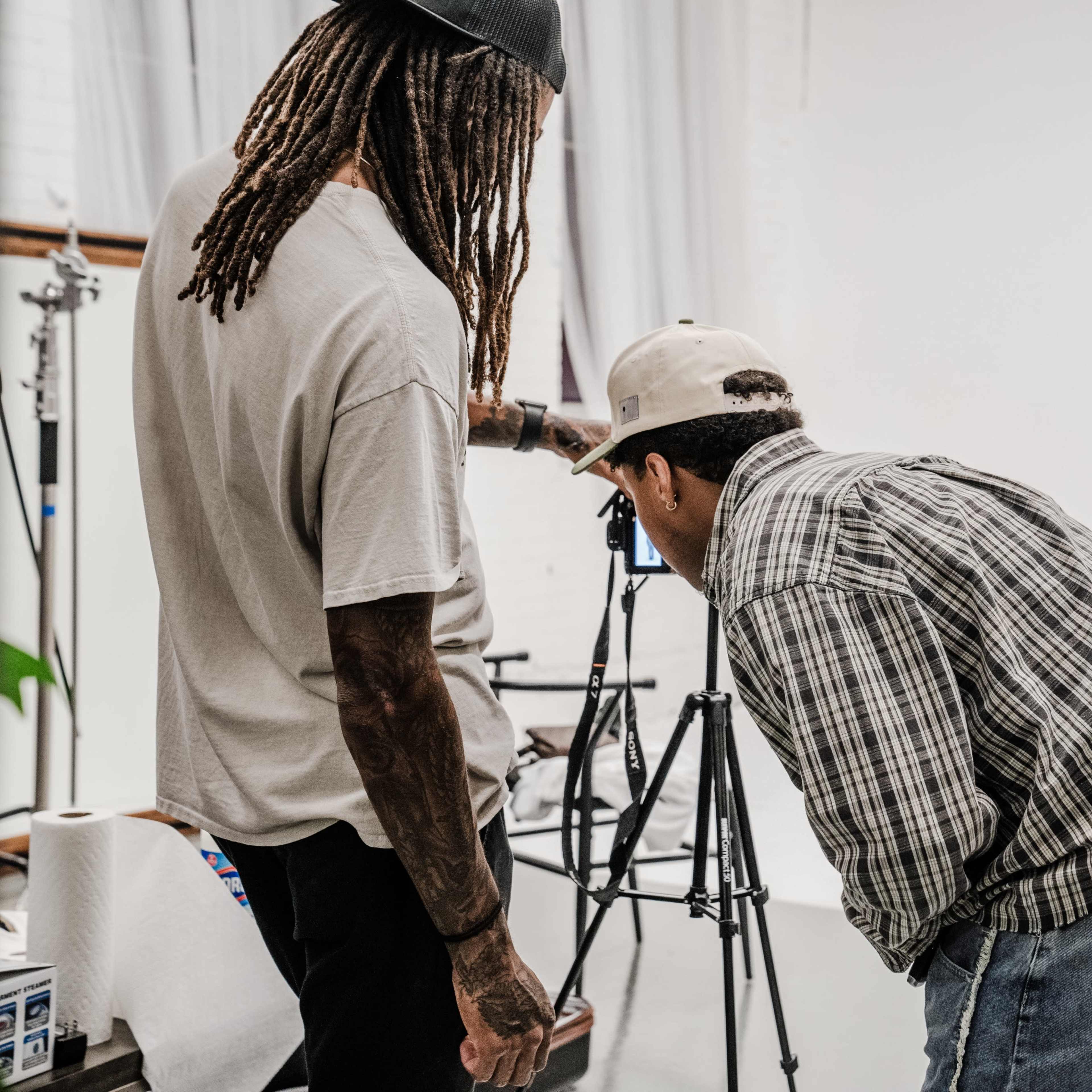 Two individuals are examining the display of a camera on a tripod in a photography studio.