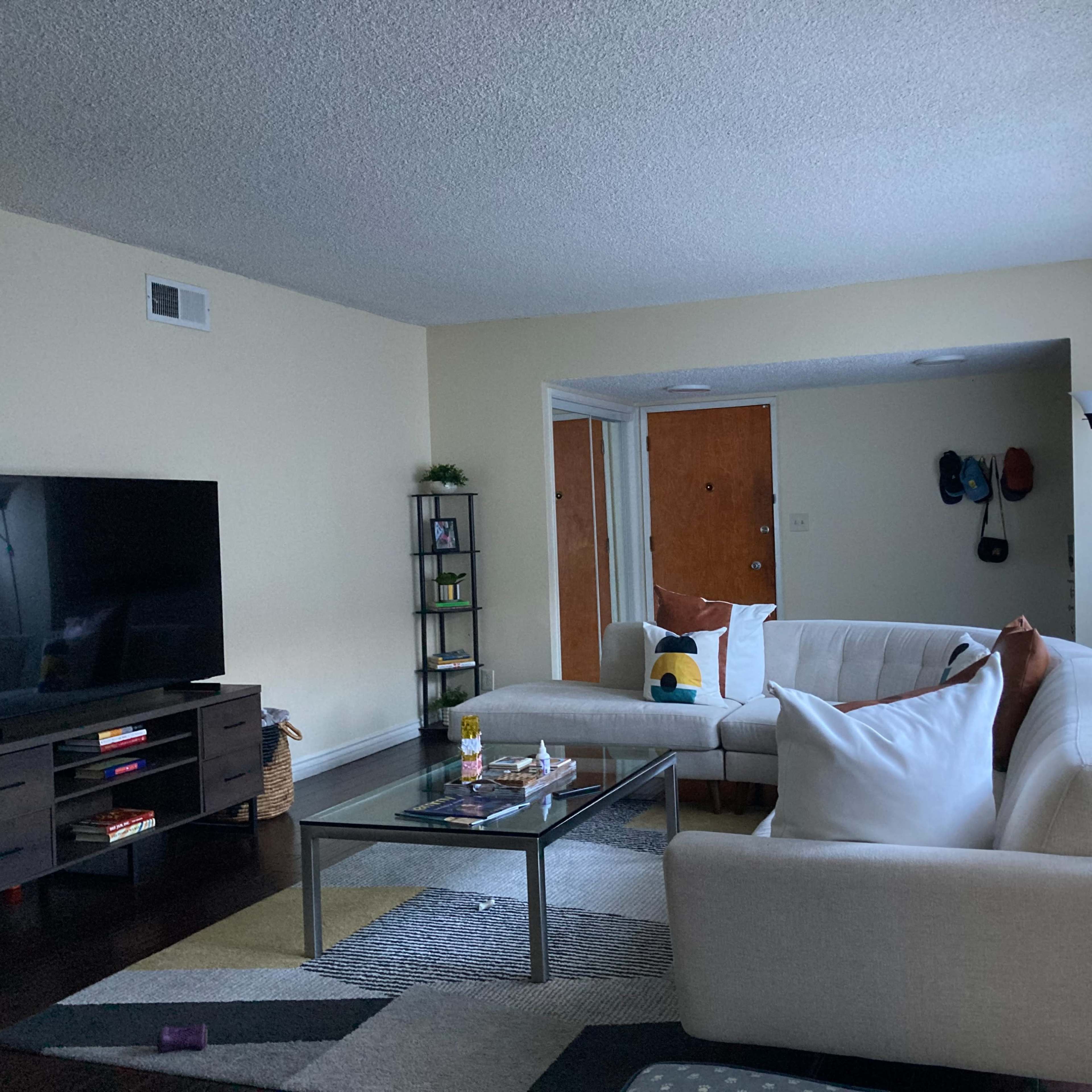A modern living room features a white sectional sofa, a glass coffee table, and a black television on a dark wood console.