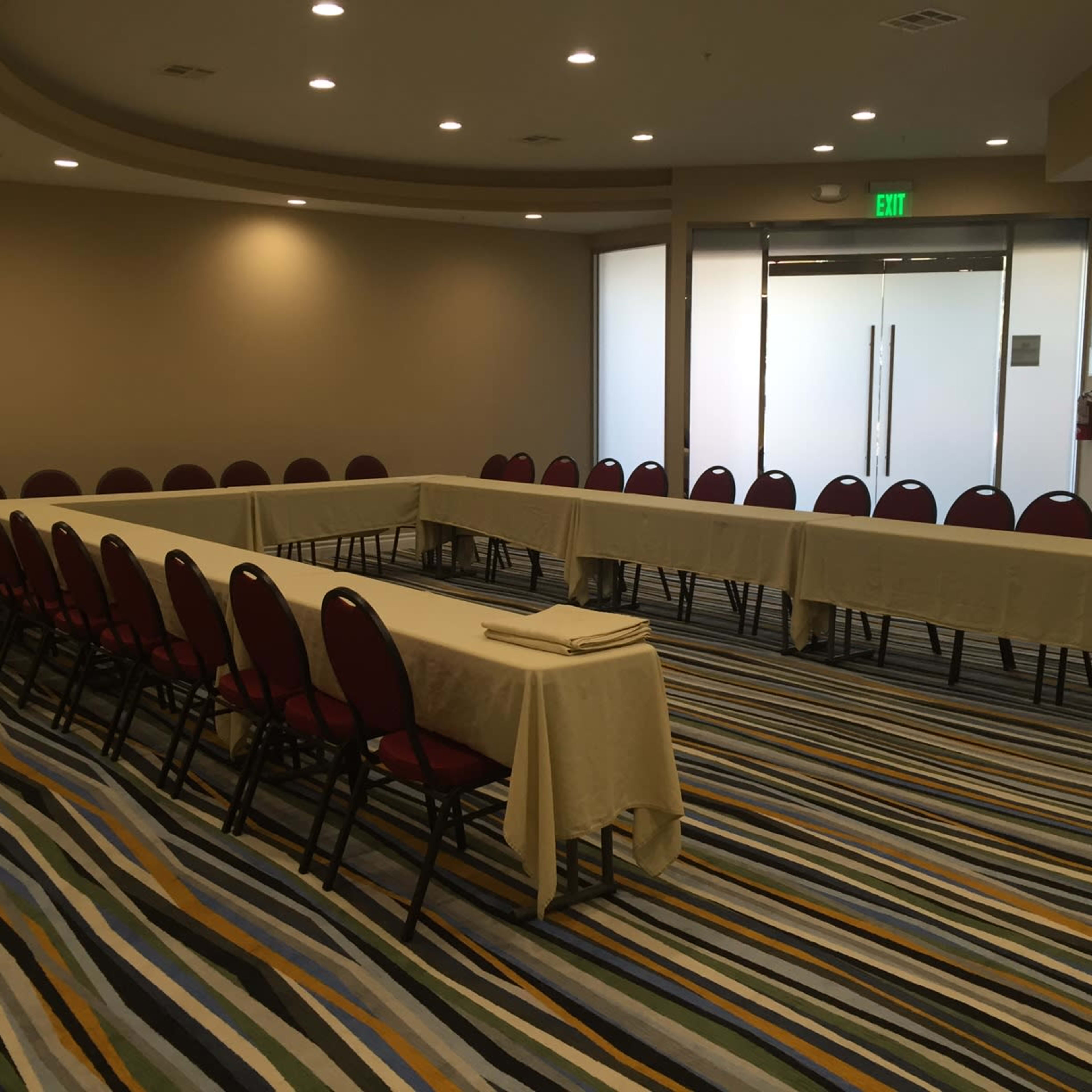 A conference room is set up with a large rectangular table surrounded by chairs and has gray and colorful striped carpeting.