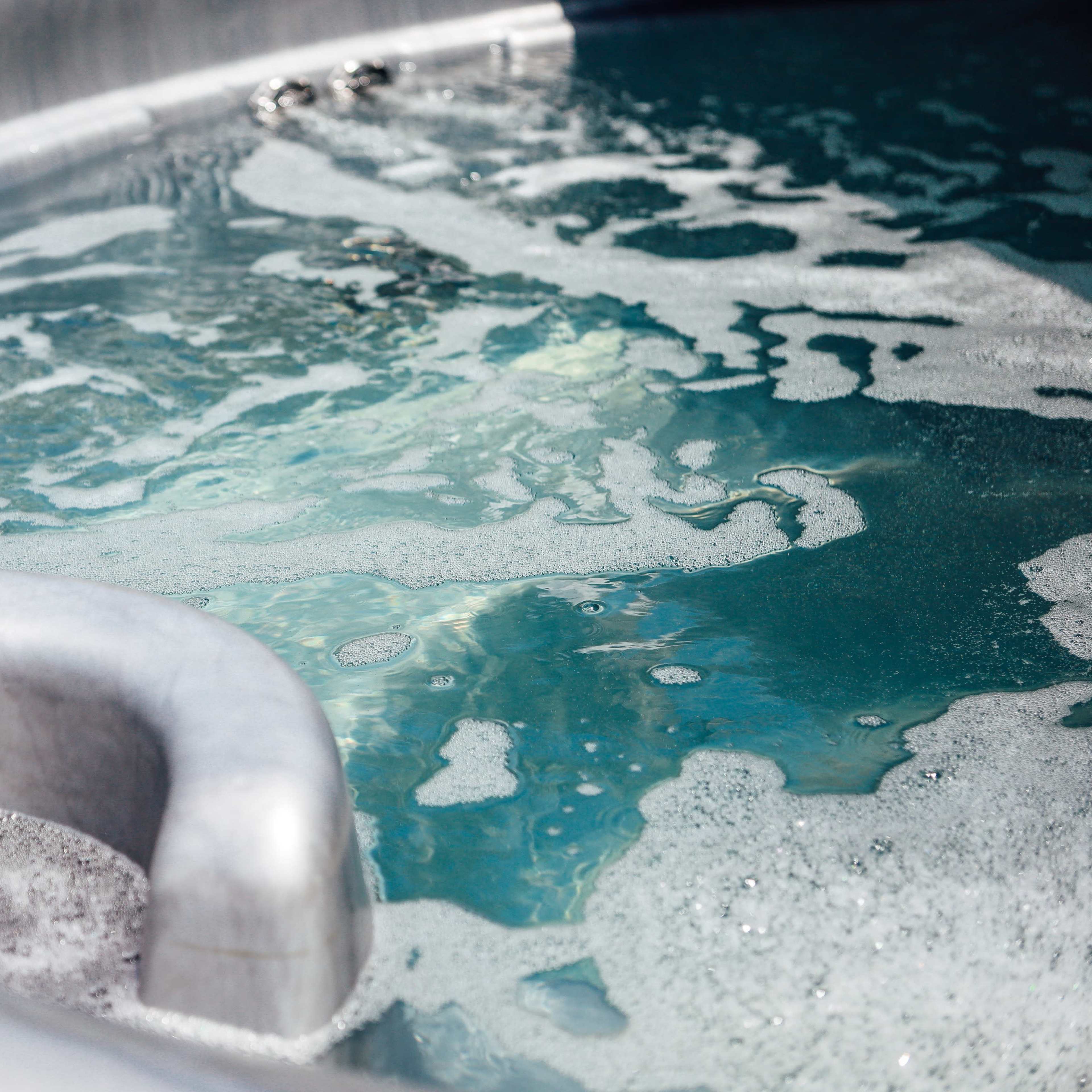 A close-up of a bubbling hot tub with silver-colored interior and clear, blue water.