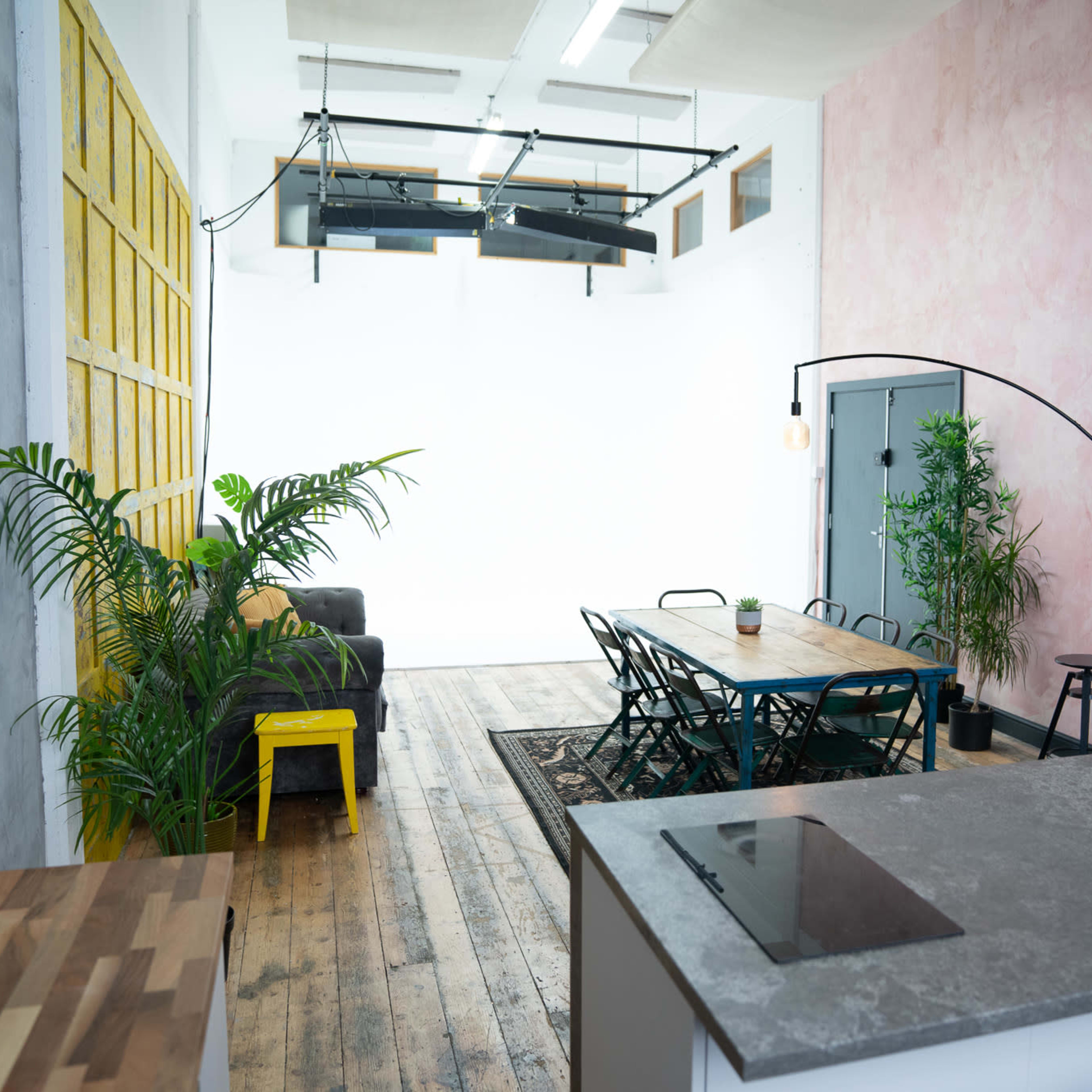 A spacious, modern open area featuring a dining table, chairs, a couch, and plants, with a polished wooden floor and distinct wall colors.