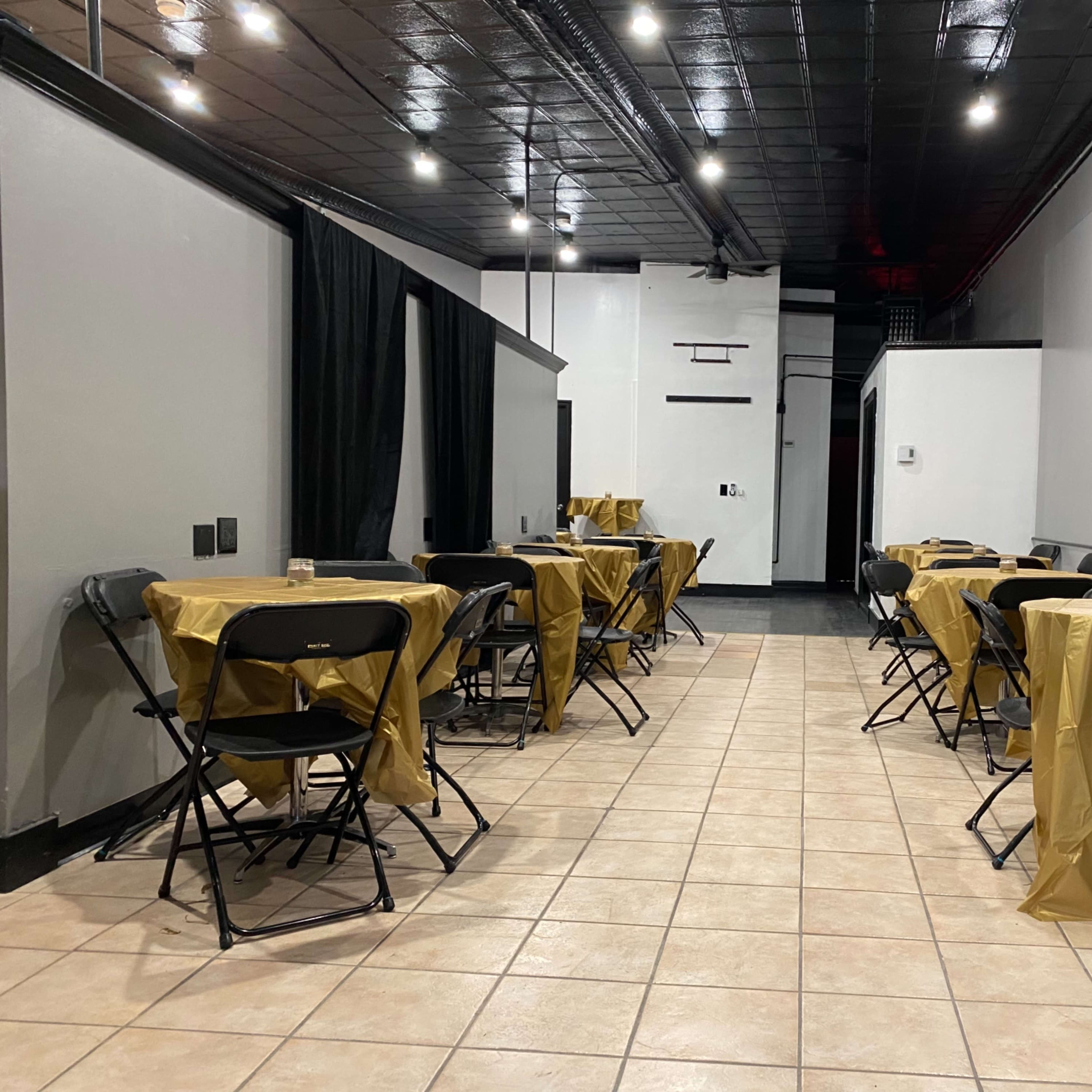 A long, narrow room with tables covered in golden tablecloths and black folding chairs arranged on either side.