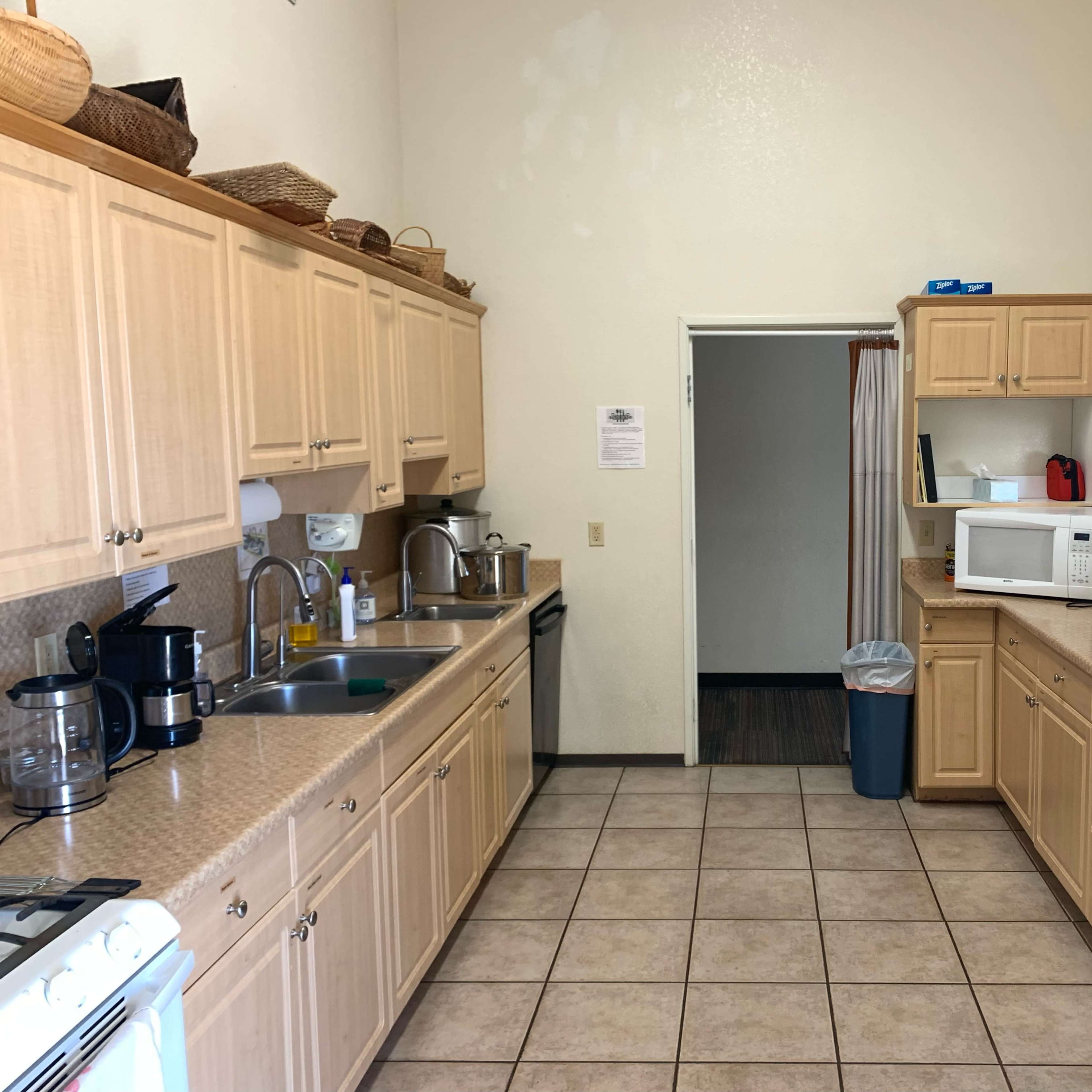 A kitchen with wooden cabinets, a countertop, and various appliances, including a microwave, coffee maker, and a trash can, arranged along the walls and counters.