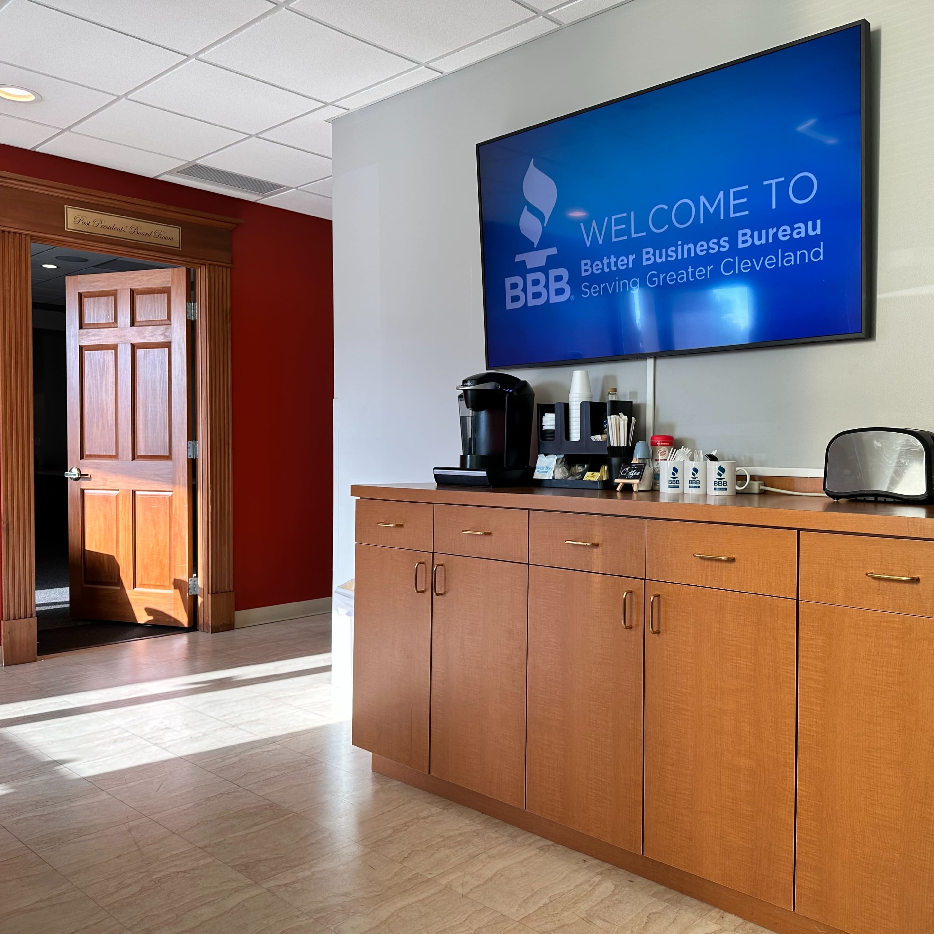A reception area with a welcome screen for the Better Business Bureau, a coffee station, and a doorway leading to another room.