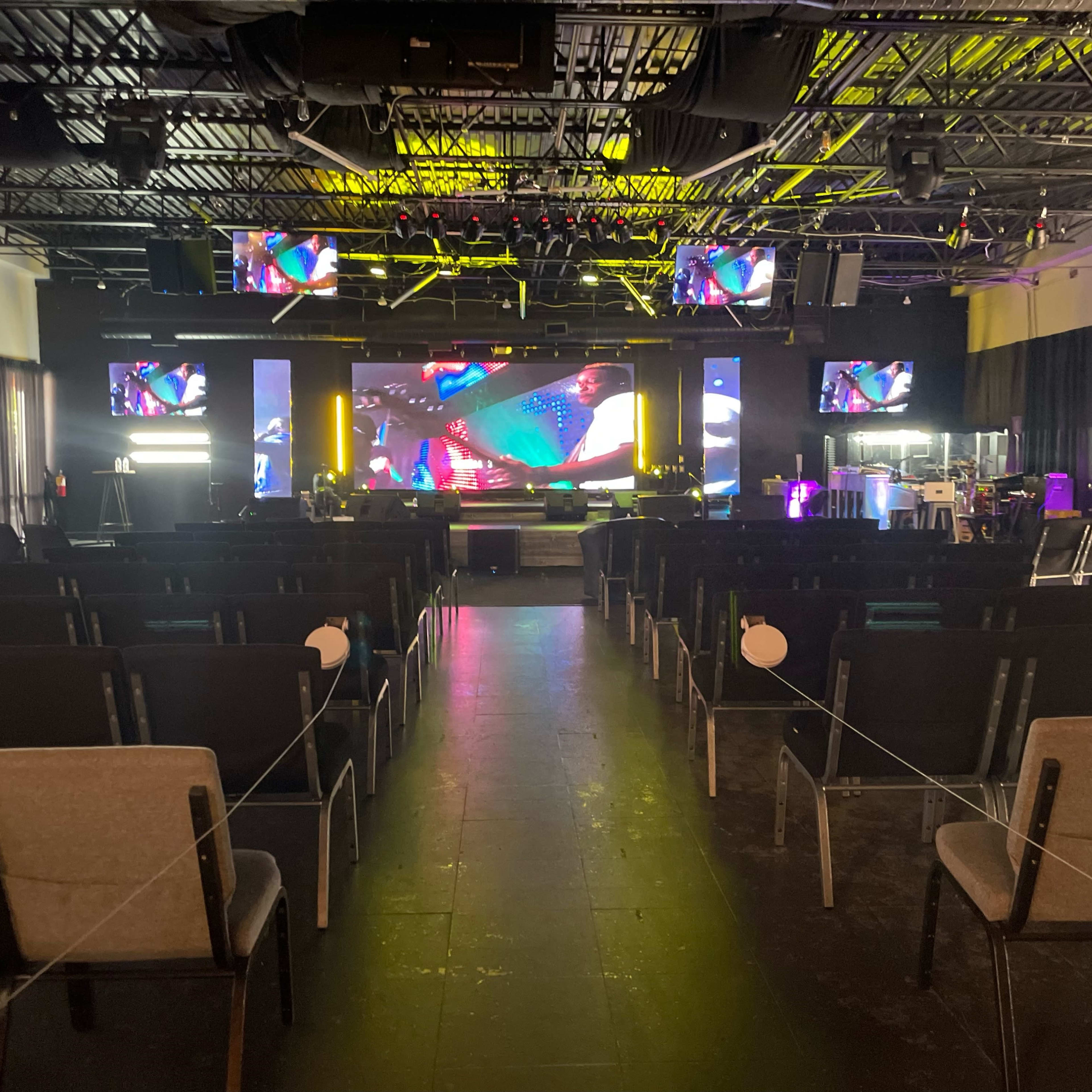 An empty event space with rows of chairs facing a stage and multiple screens displaying vibrant graphics.