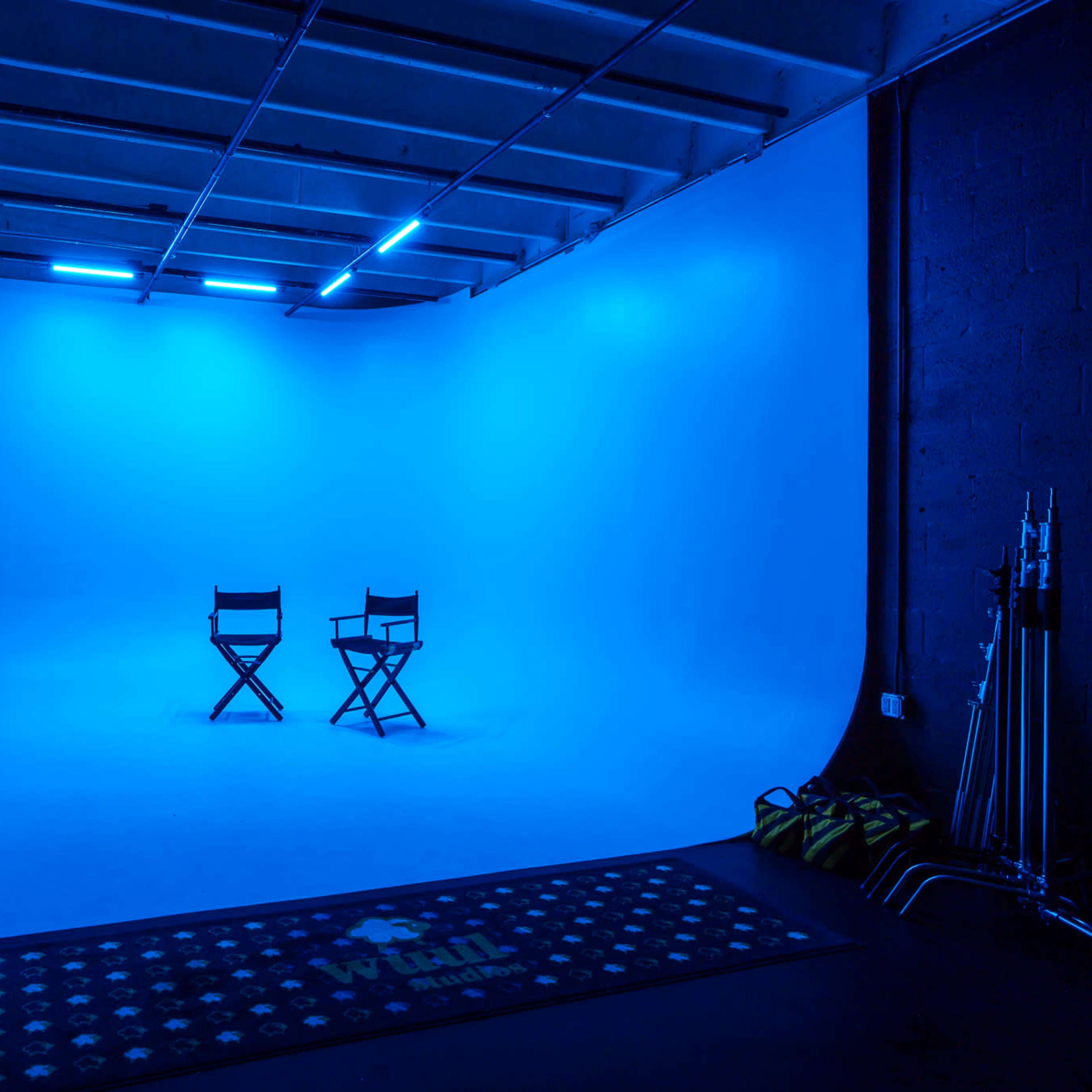 A bright blue photography studio features two director's chairs in front of a smooth backdrop.