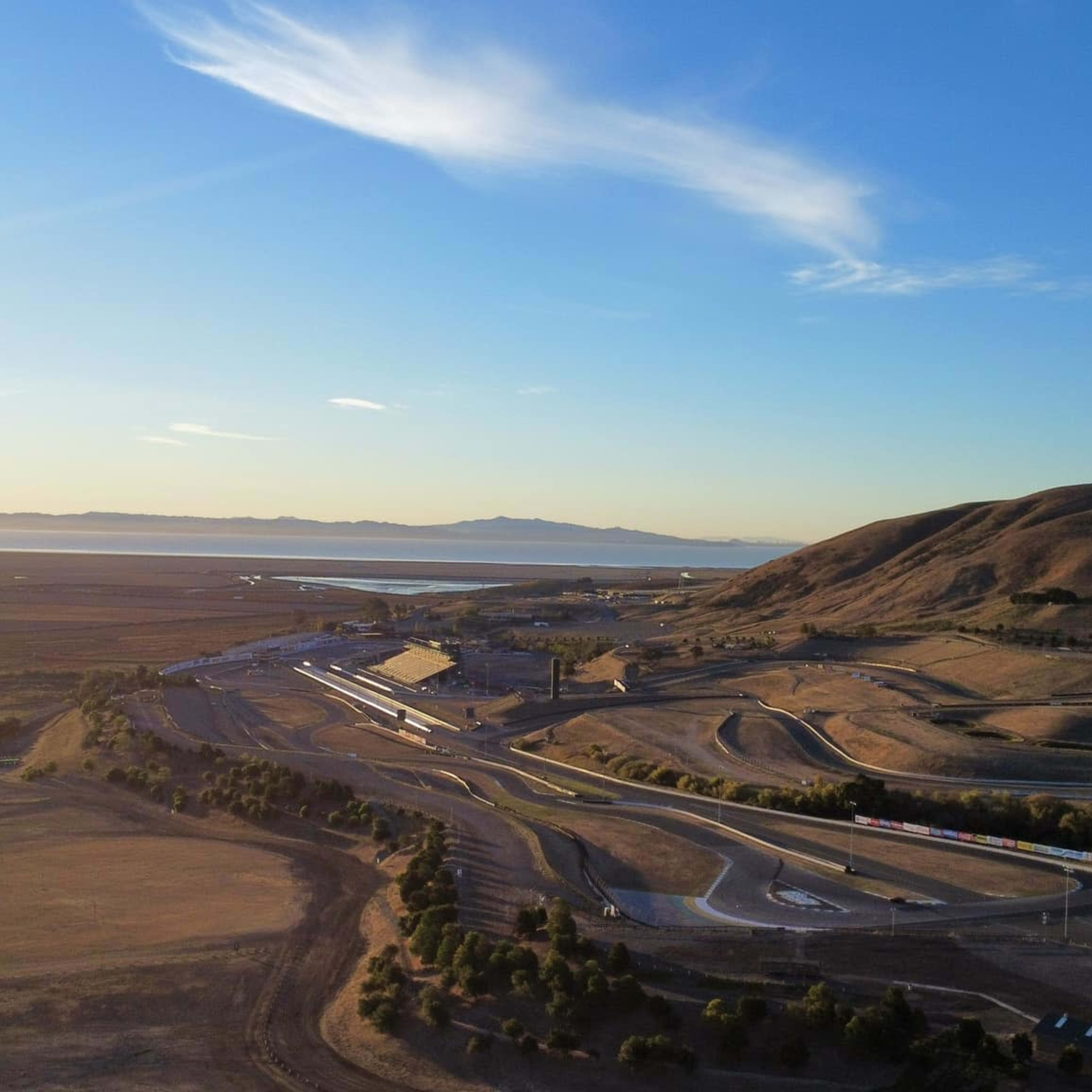 A wide view of a motorsport racetrack situated in a dry, hilly landscape with a hot air balloon in the sky above.
