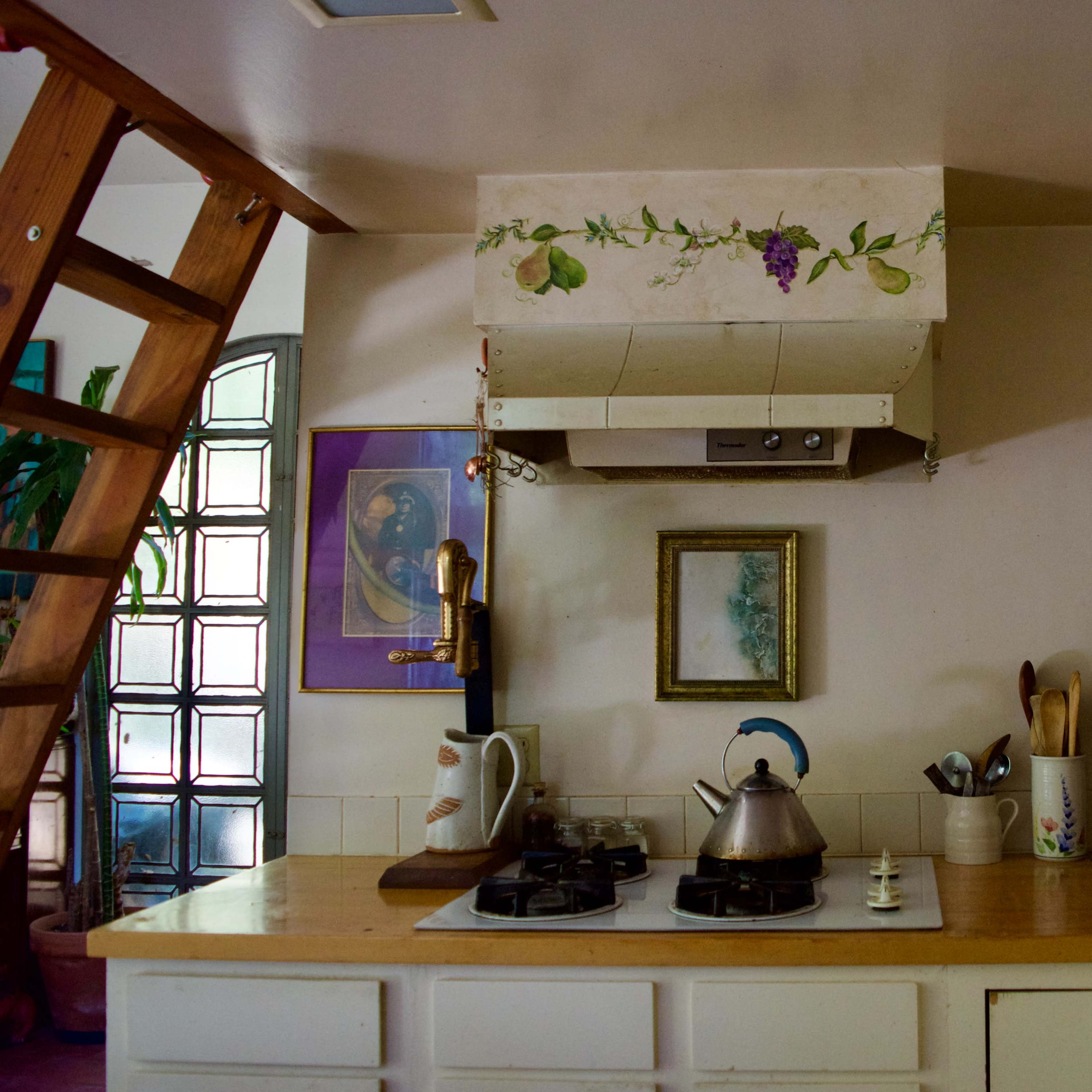 A cozy kitchen with a wooden countertop, a gas stove, a kettle, and shelves containing various kitchen utensils and decorations.