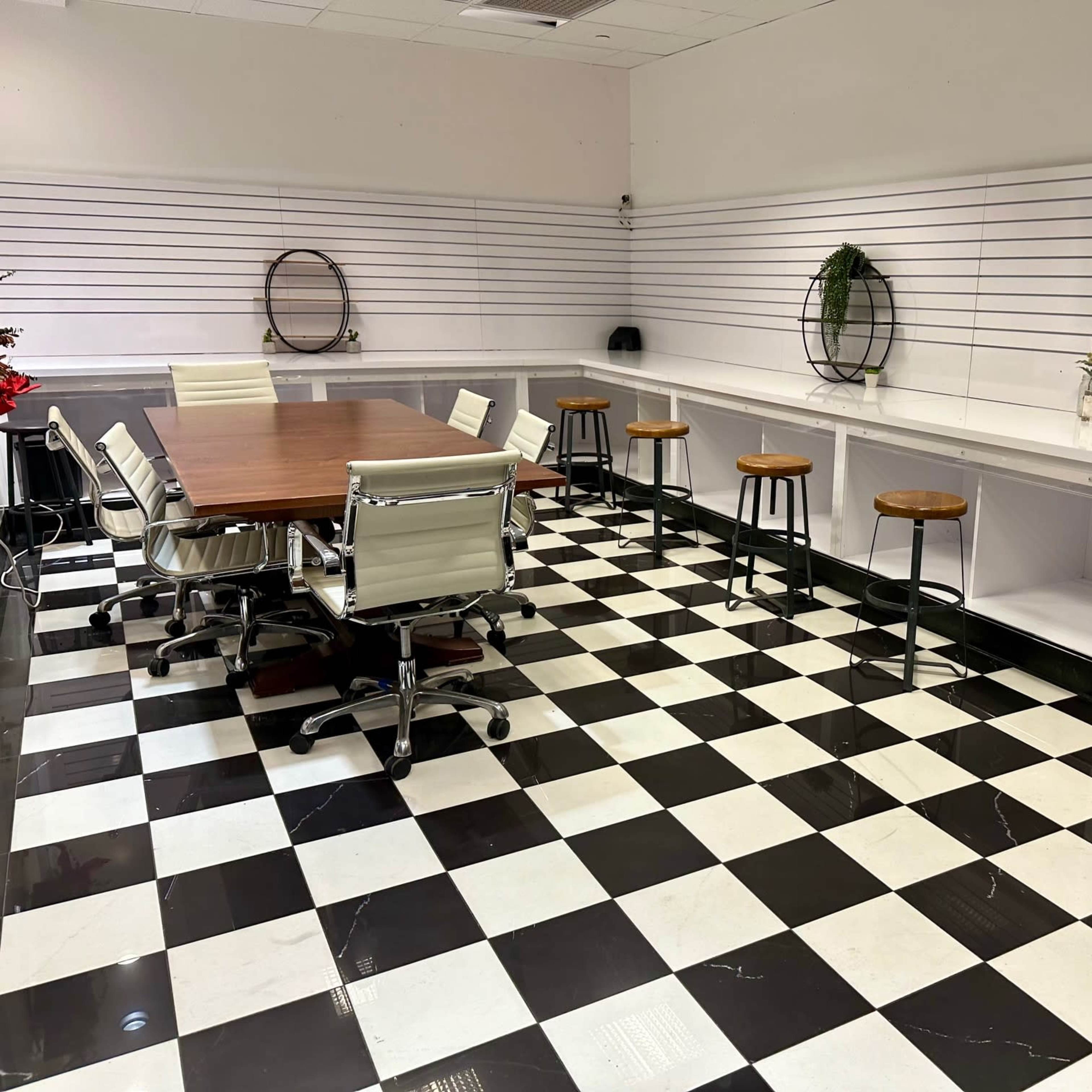 The room features a large wooden table surrounded by white chairs, with bar stools along a counter, all set on a black and white checkered floor.