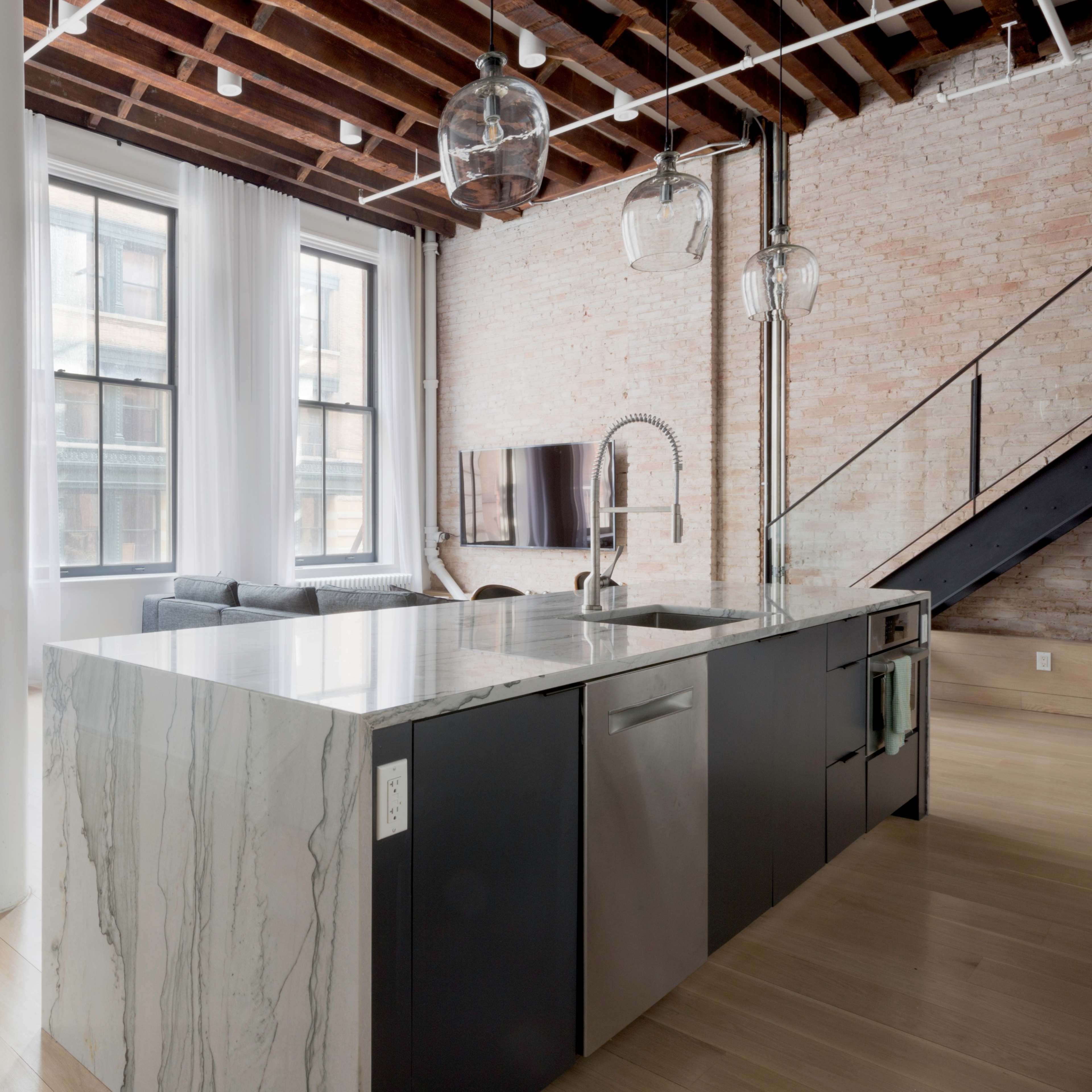 A modern kitchen with a large marble island and stainless steel appliances, adjacent to a dining area with wooden chairs and a table in a loft-style setting.
