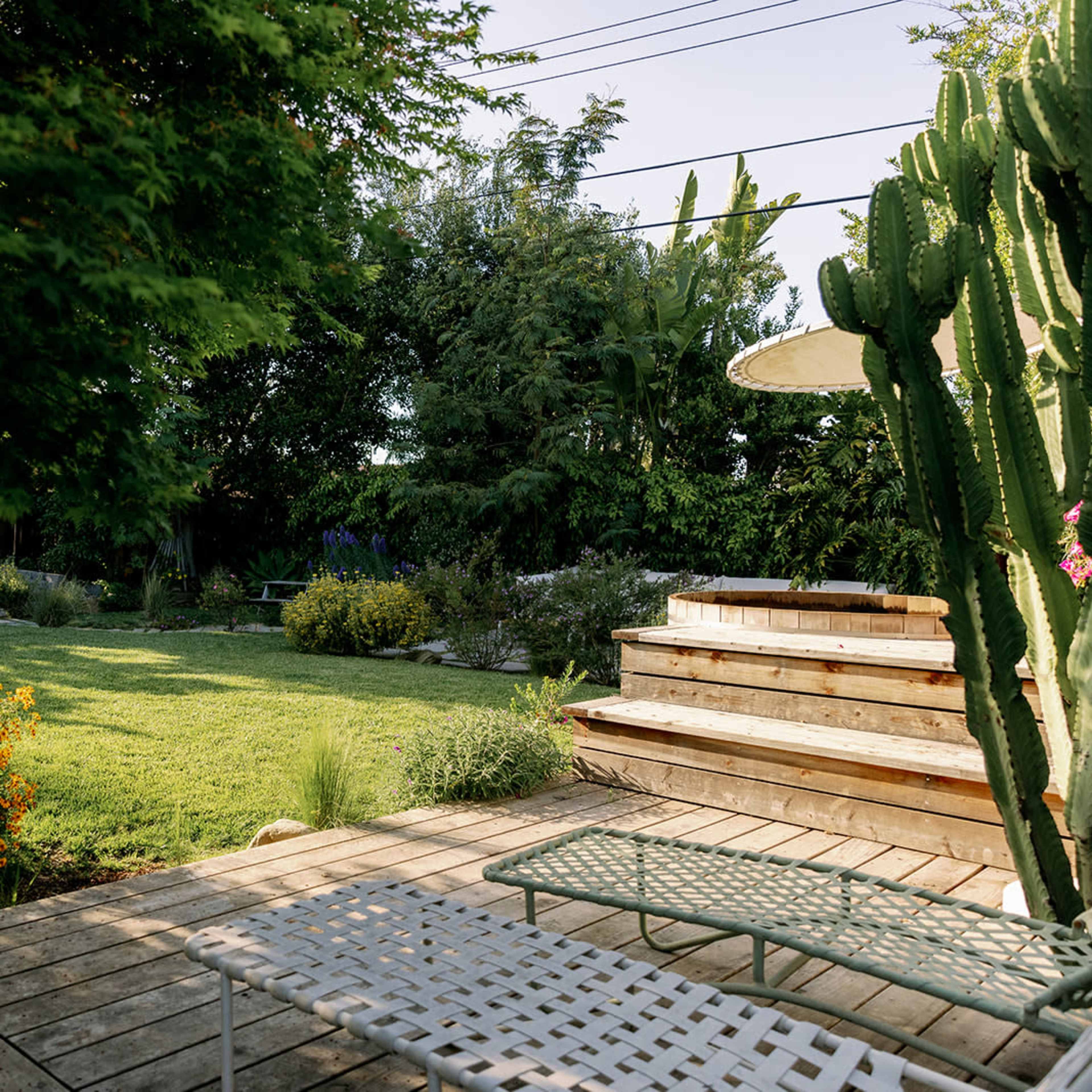 A landscaped backyard featuring a wooden deck, lounge chairs, and a grassy area surrounded by various plants and trees.