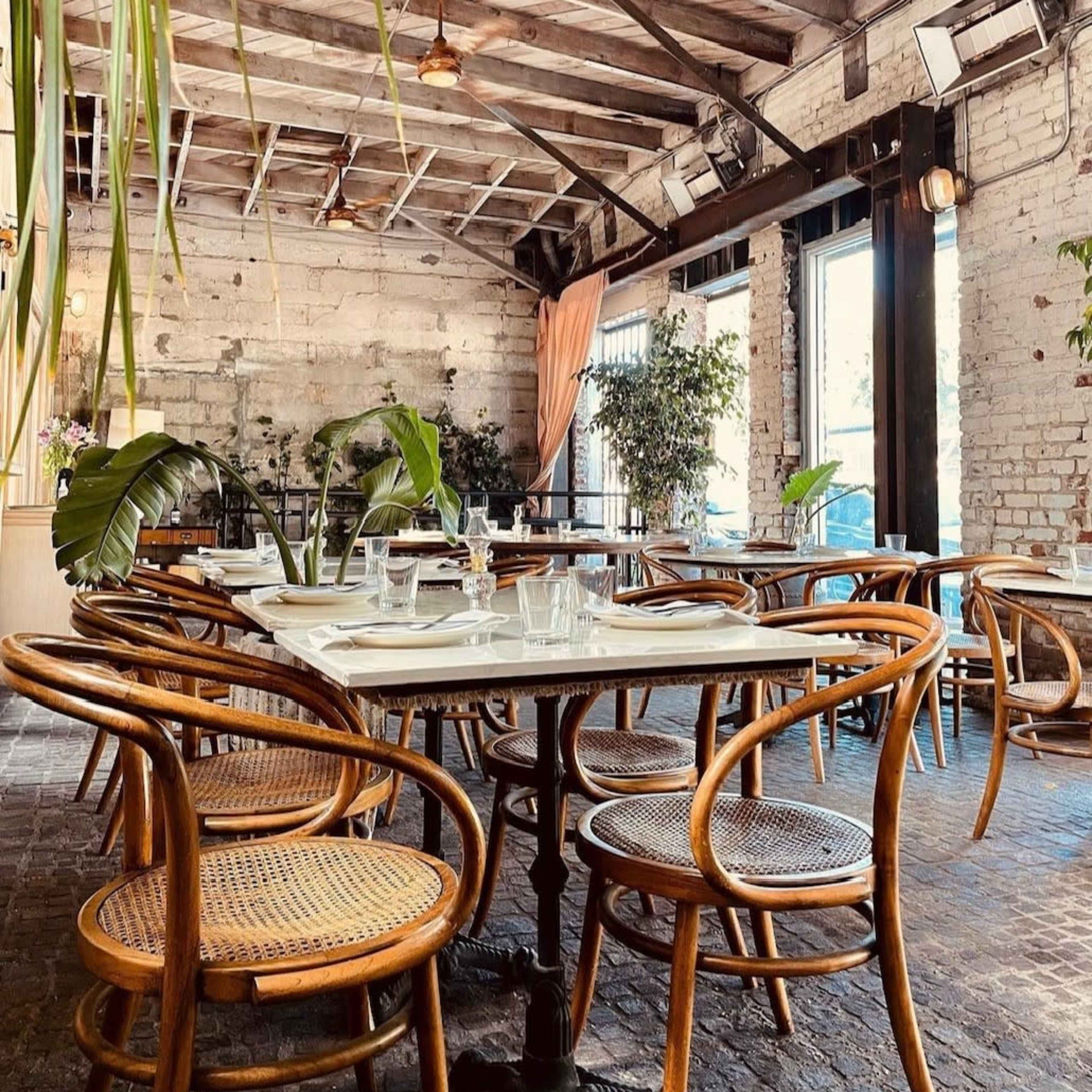 A cozy restaurant interior with wooden beams, wicker chairs, and tables set for dining.