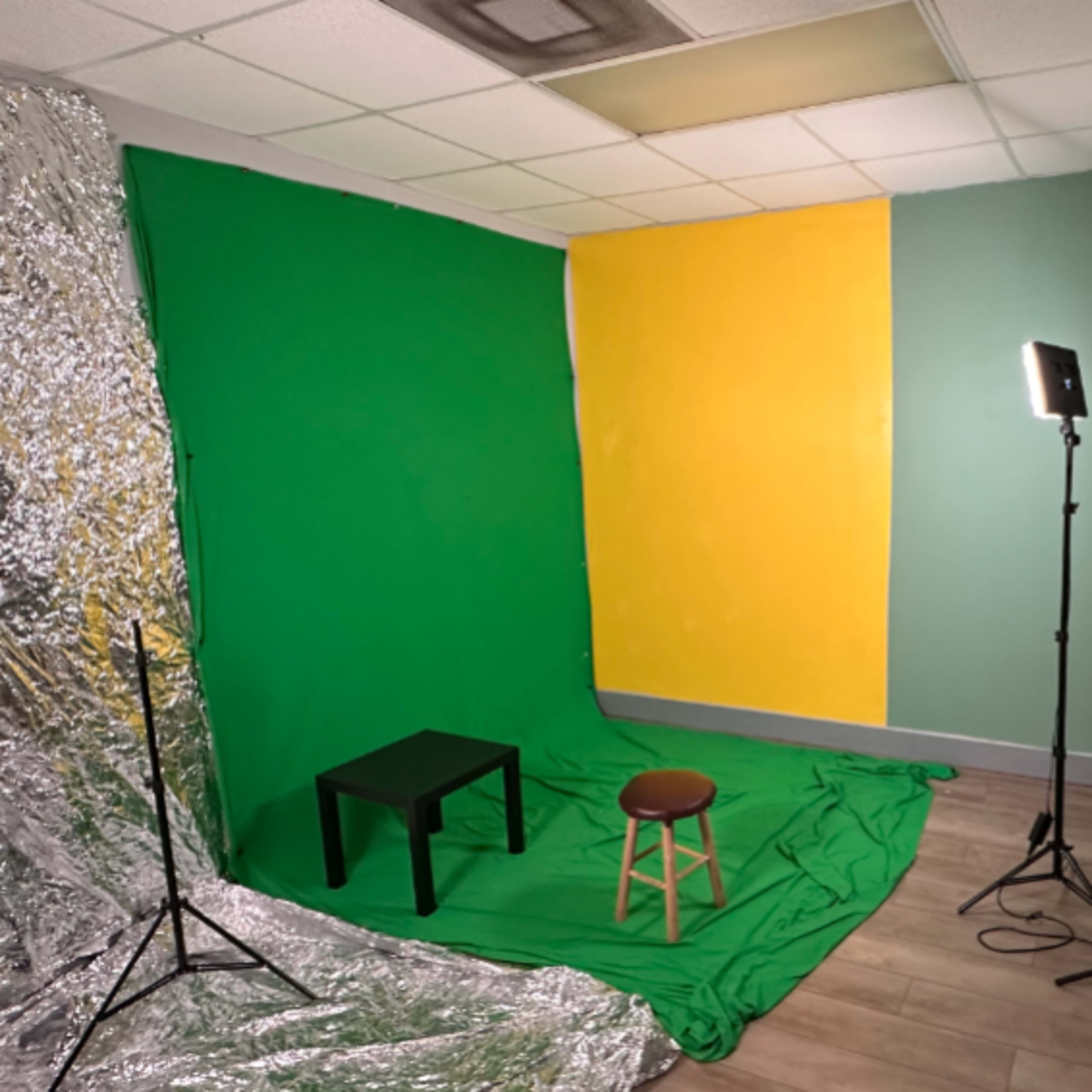 A small studio setup with green and yellow backdrops, a table, a stool, and lighting equipment.