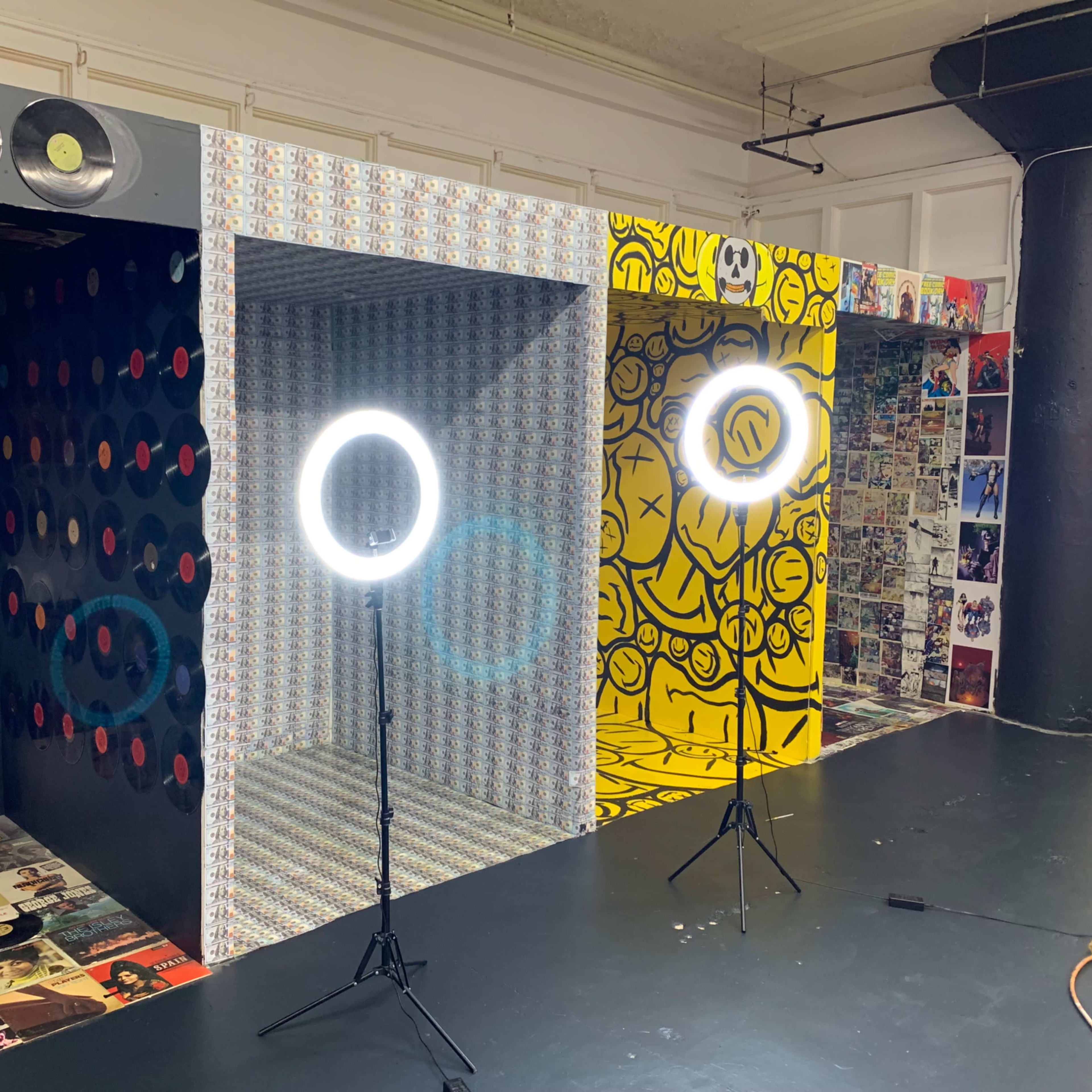 A room with three decorated walls featuring colorful patterns and graphics, with two ring lights set up on stands in front.
