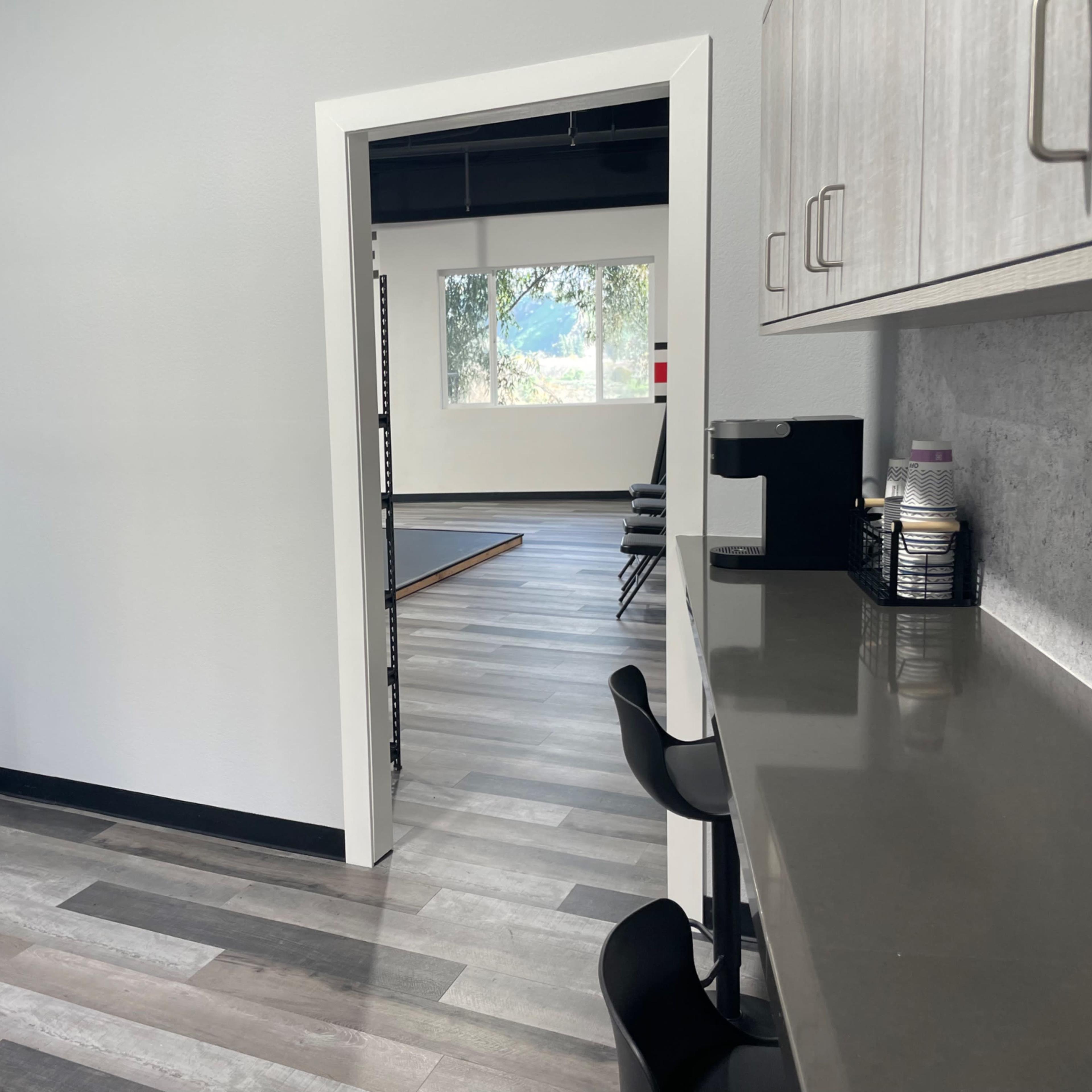 A doorway leading into a spacious, light-filled room with a kitchenette area featuring black bar stools and a countertop.
