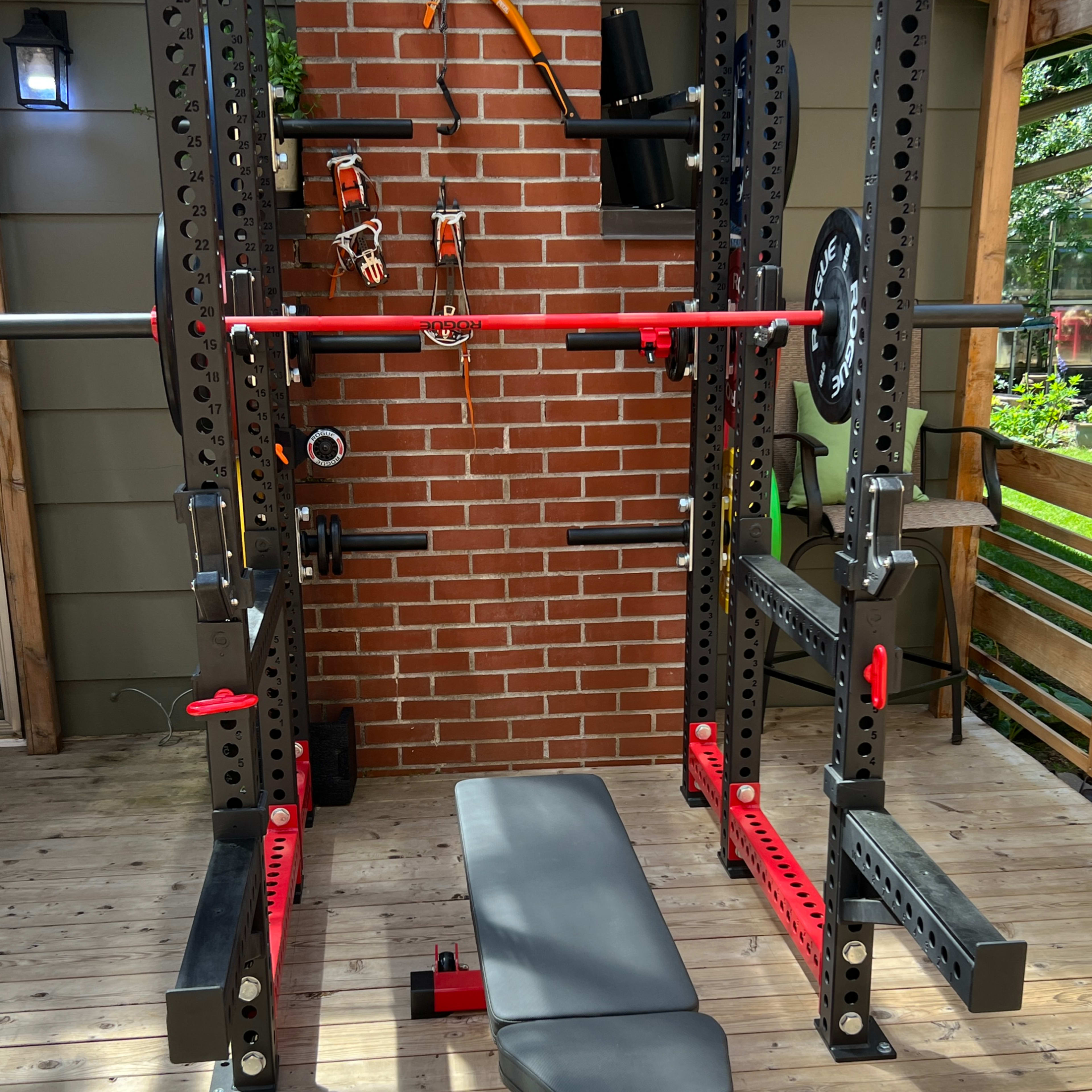 A weightlifting setup with a squat rack, bench, and various accessories against a brick wall in a wooden structure.