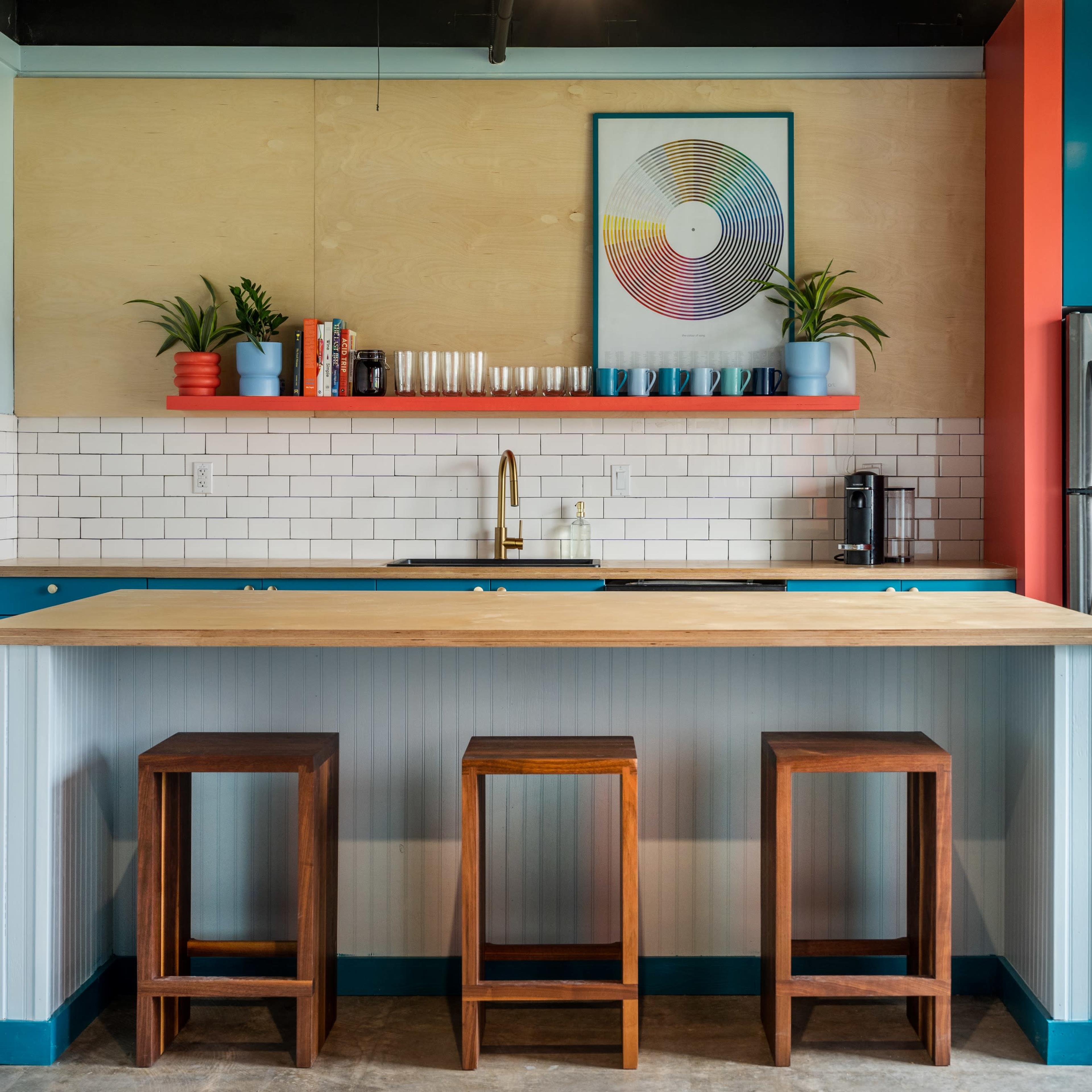 A modern kitchen features a wooden island with three wooden stools, colorful cabinets, and a stainless steel refrigerator.