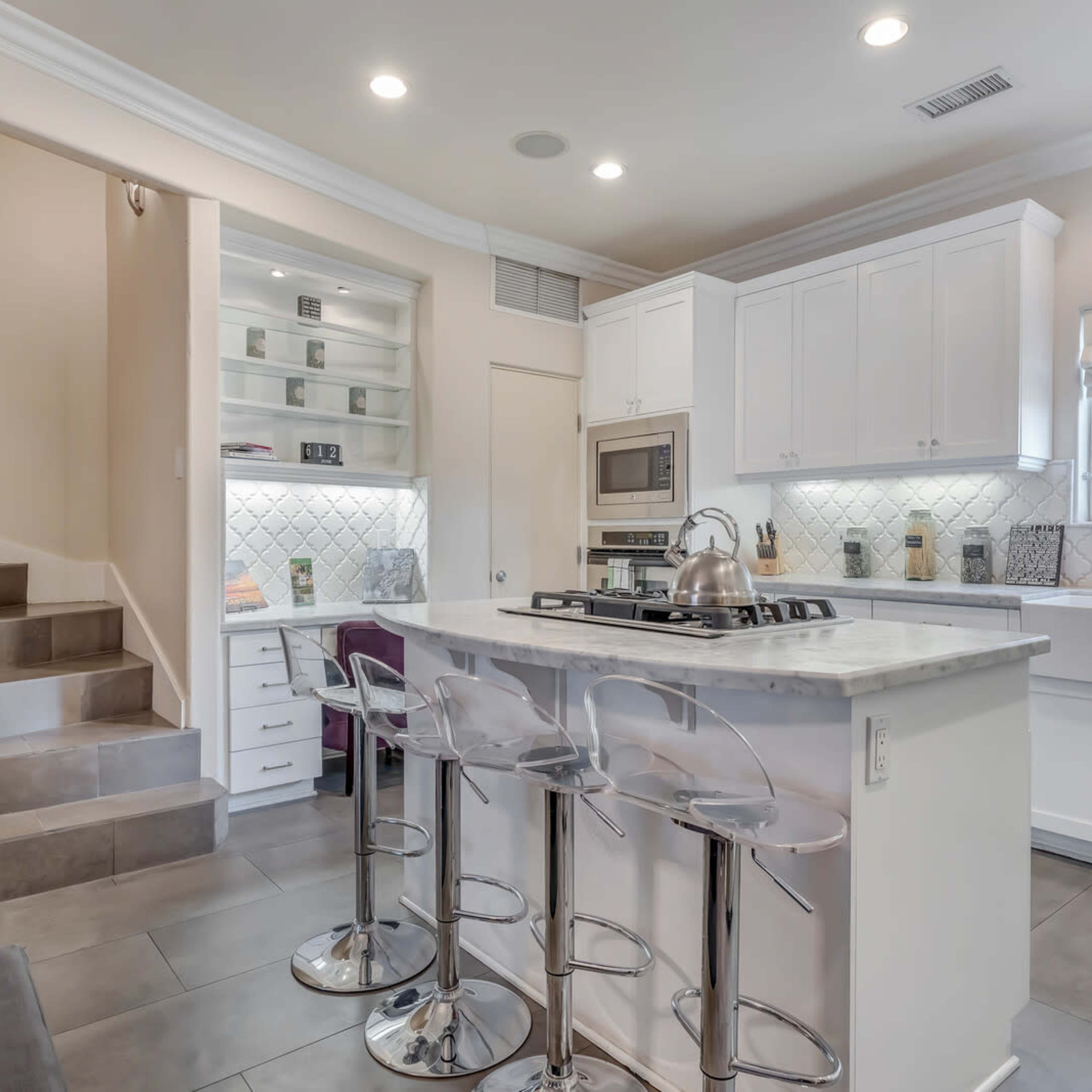 A modern kitchen with a white island, bar stools, and a staircase leading to an upper level.