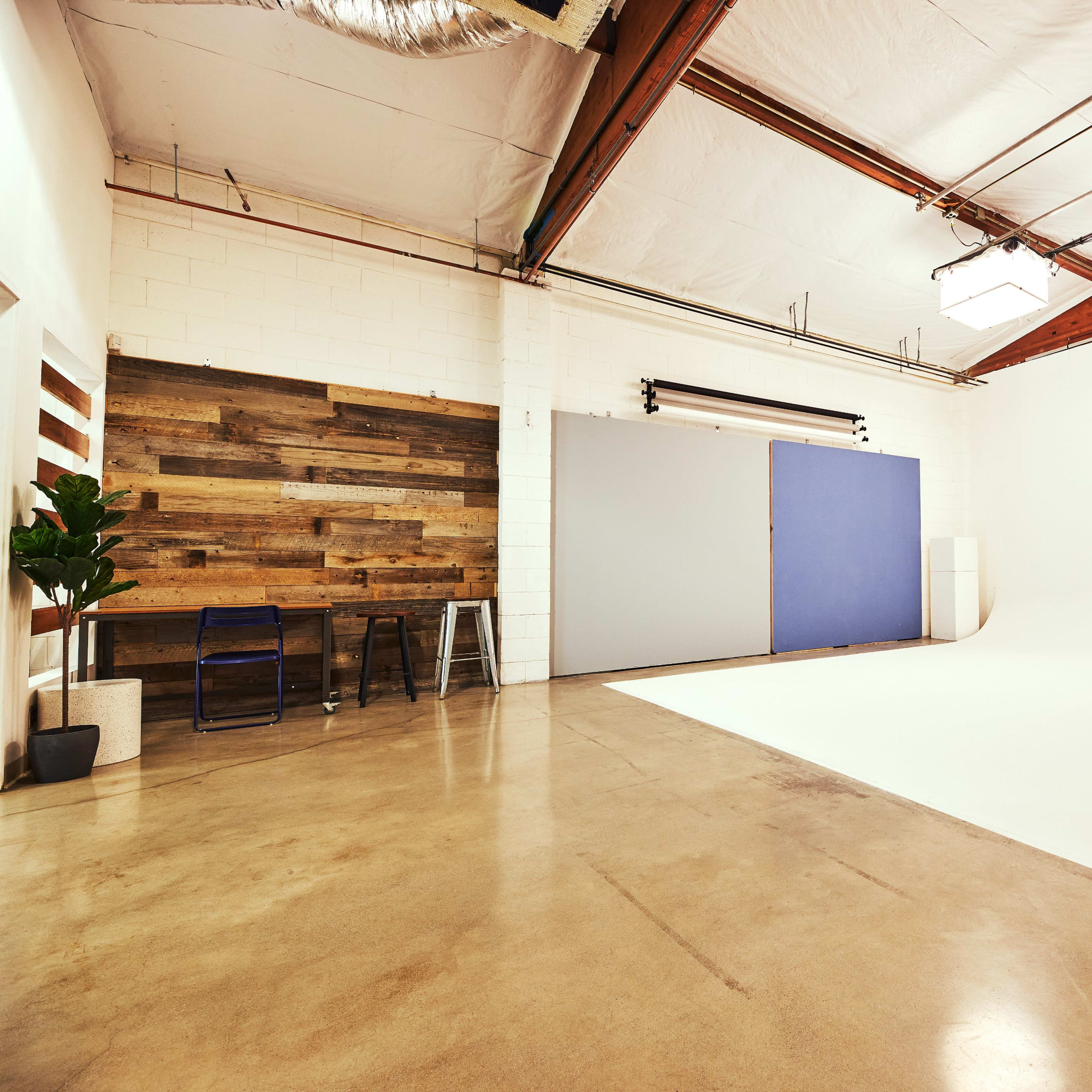 A spacious photography studio with a seamless white backdrop, wooden accent wall, industrial lighting, and concrete flooring.