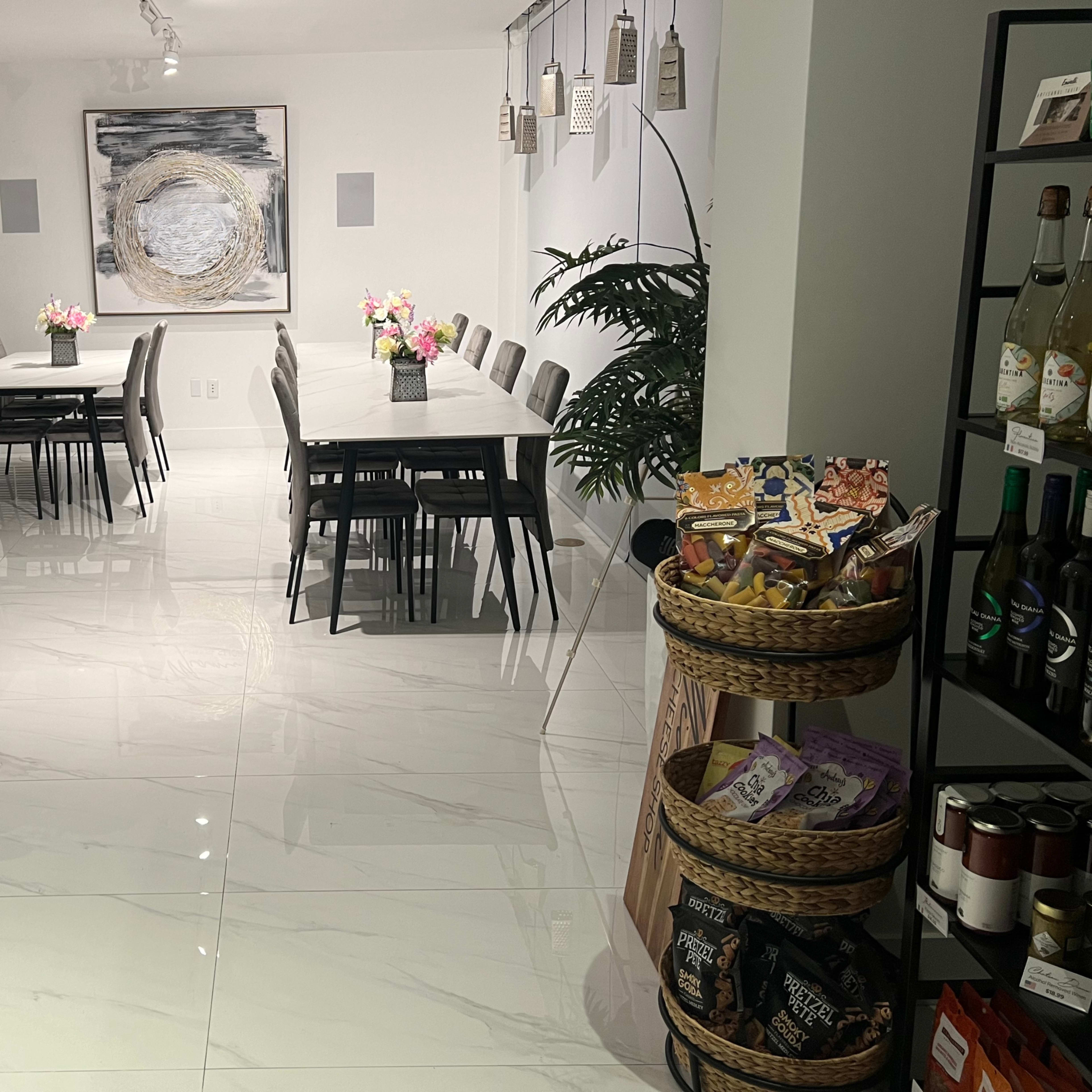 A modern dining area features white tables and chairs, a glass display case, a large wall art piece, and shelves of drinks and snacks.