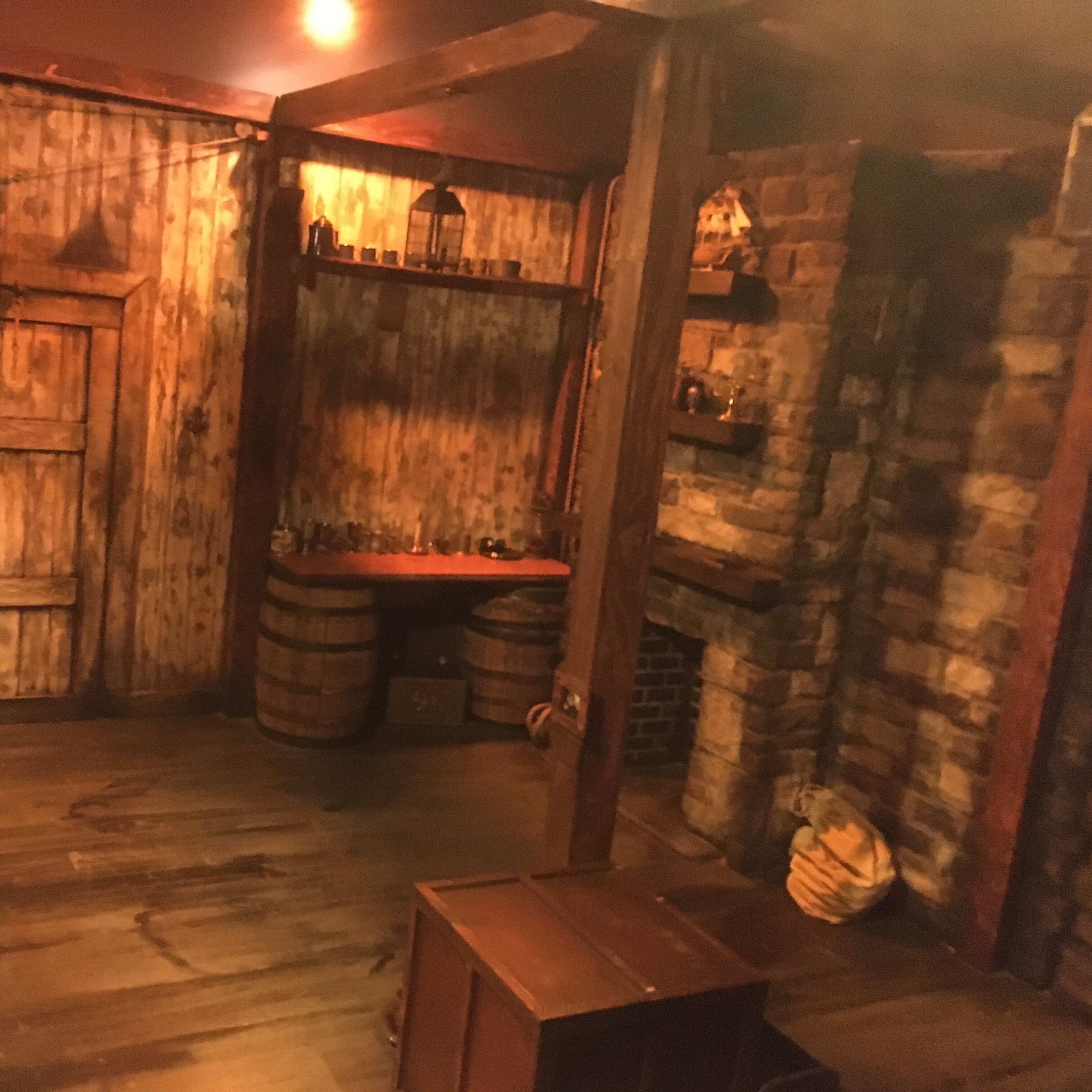 A rustic, dimly lit room with wooden walls, barrels, and a closed door.