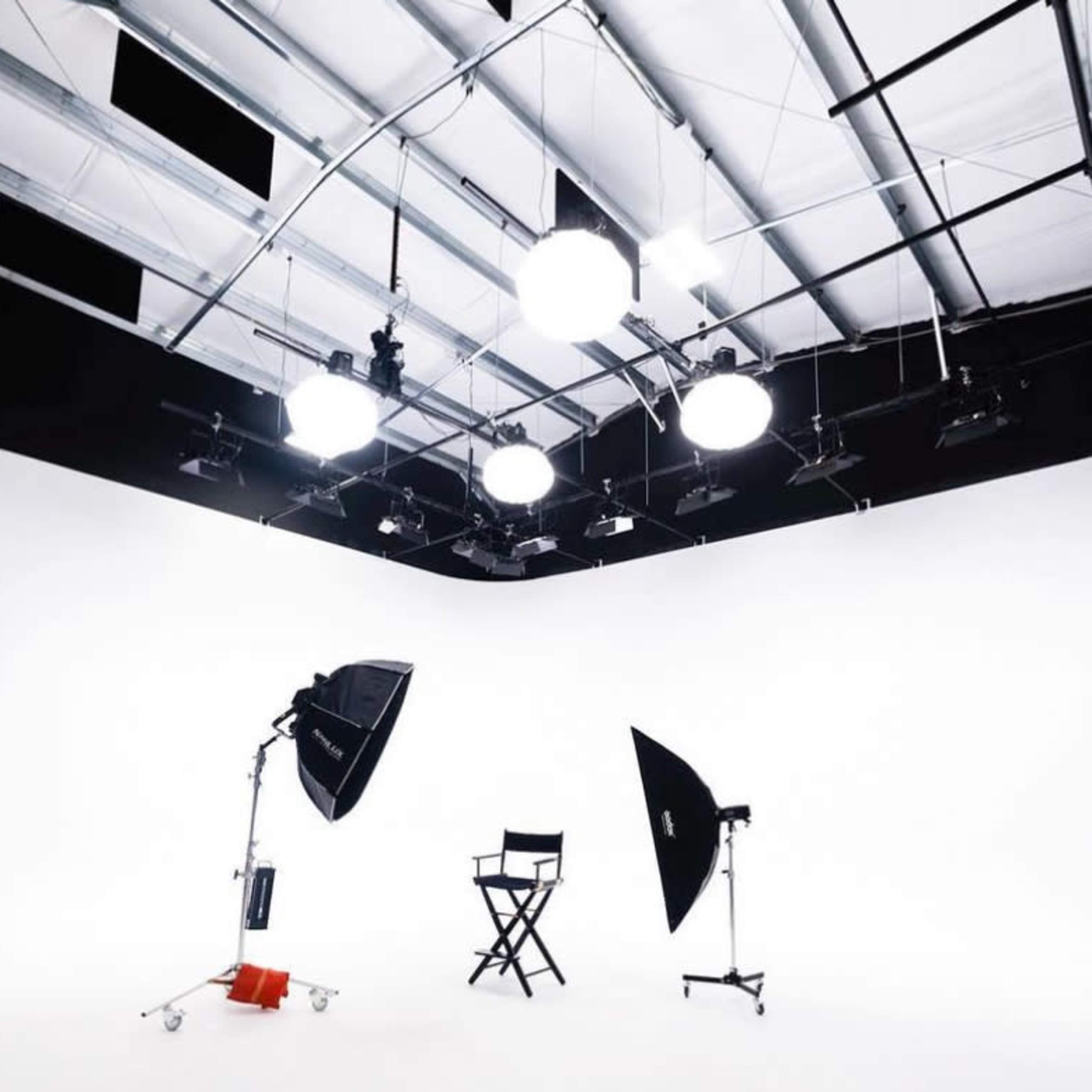 A photography studio features a white background, a director's chair, and multiple lighting equipment arranged around the space.