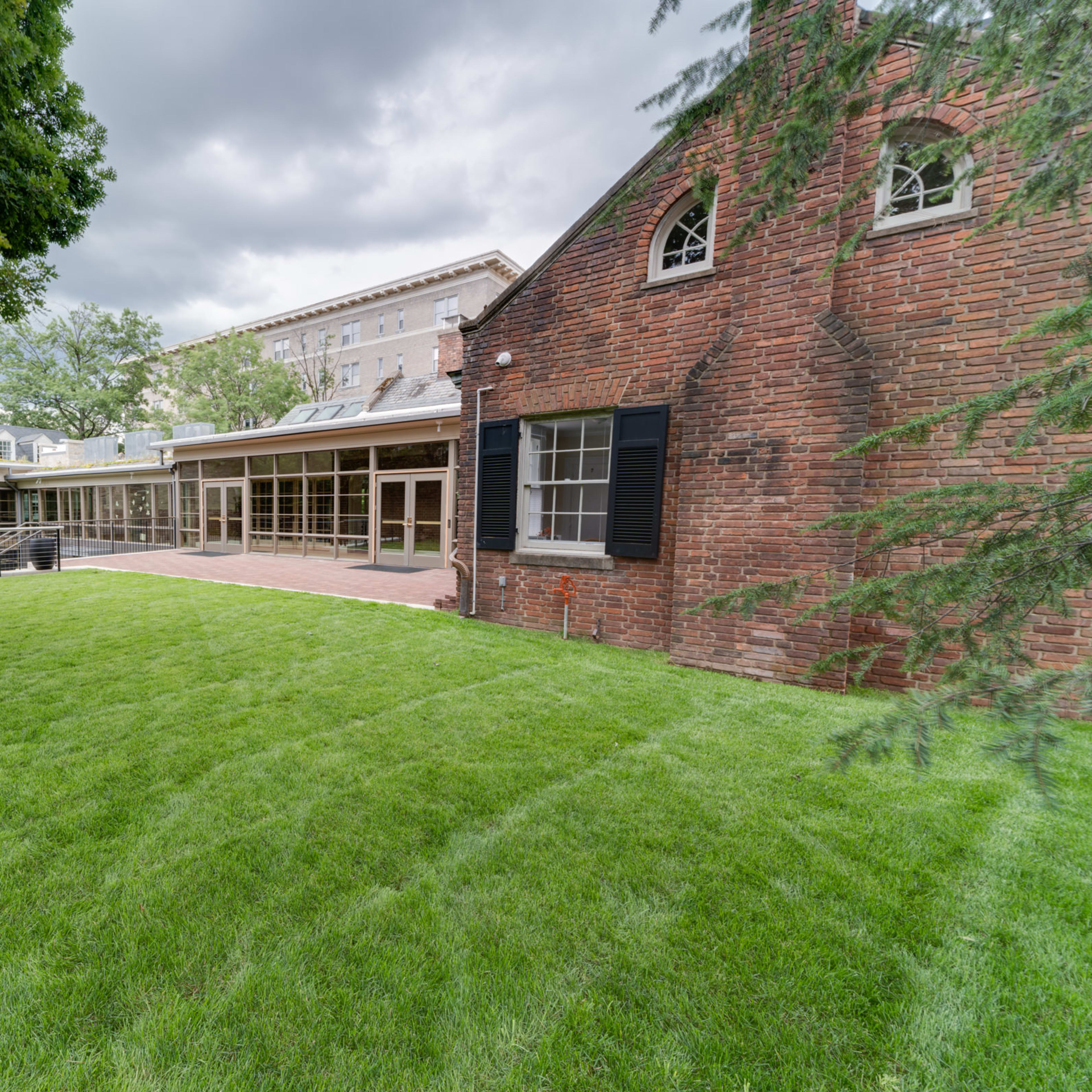 A grassy lawn surrounded by brick and stone buildings under a cloudy sky.